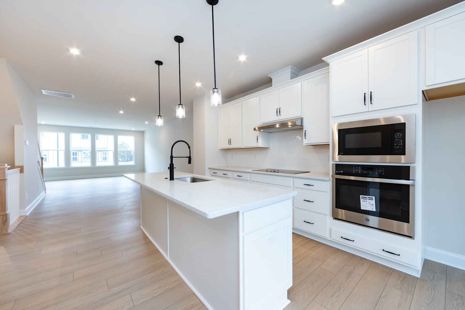 A modern, open-concept kitchen with white cabinets, stainless steel appliances, and pendant lighting, leading into a bright and airy living space with hardwood floors.