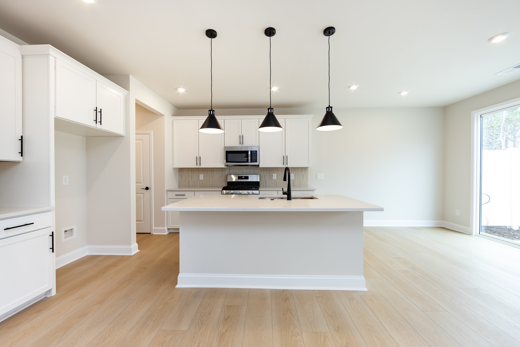 A modern, open-concept kitchen with white cabinets, a central island, and three black pendant lights hanging above the island.