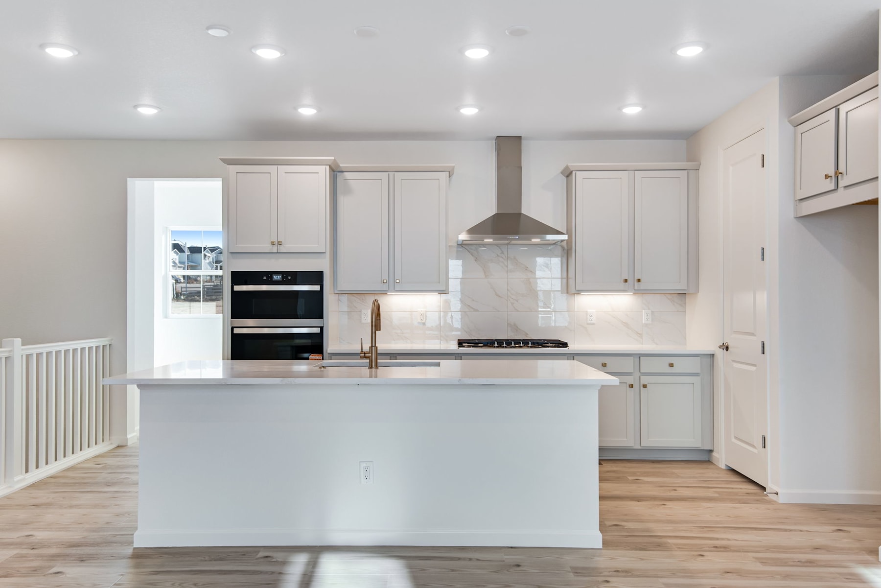 A modern, bright kitchen with white cabinets, a central island, and hardwood floors.