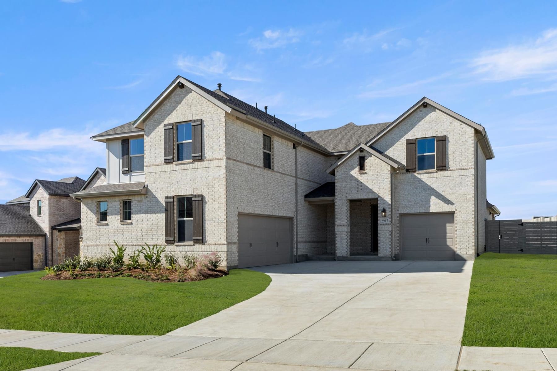 A large, two-story house with a gray exterior and a well-manicured lawn in the foreground, set against a clear blue sky with some clouds.