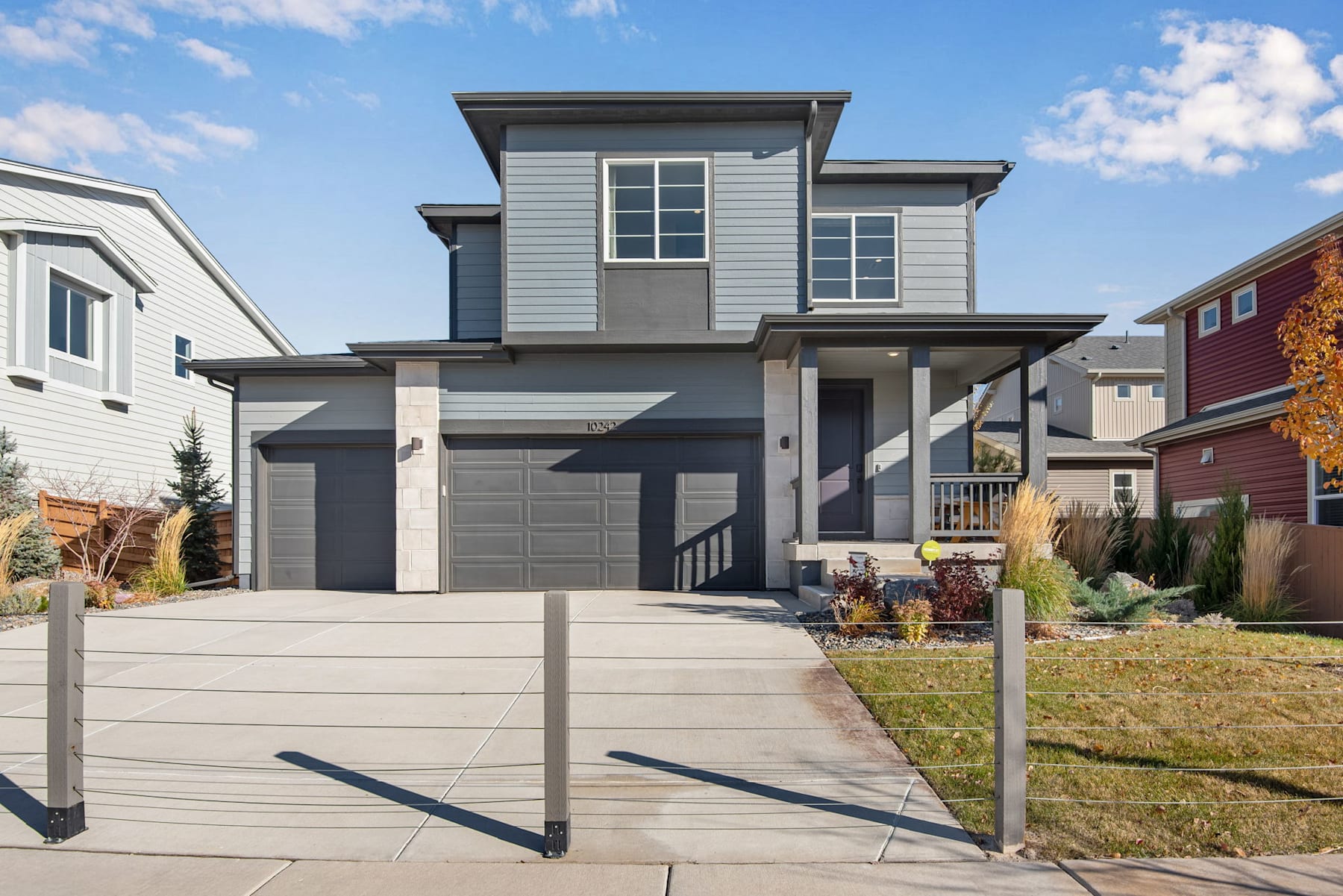 A modern two-story house with a gray exterior, a garage, and a well-maintained yard with a paved walkway leading to the front entrance, set against a backdrop of a clear blue sky with scattered clouds.