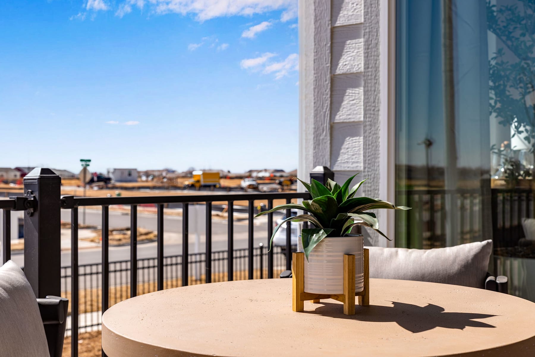 A cozy outdoor balcony with a round table, a potted plant, and a view of the city skyline in the background.