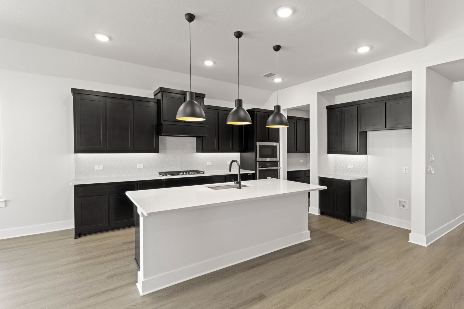 A modern, minimalist kitchen with dark cabinets, a white island, and pendant lights hanging from the ceiling.