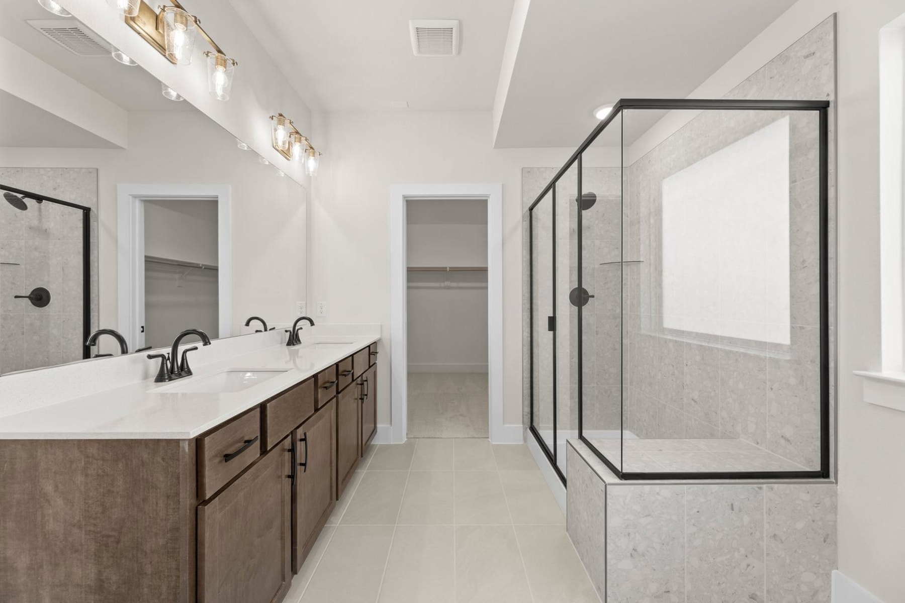 A modern and spacious bathroom with a double vanity, a large glass-enclosed shower, and recessed lighting fixtures on the ceiling.