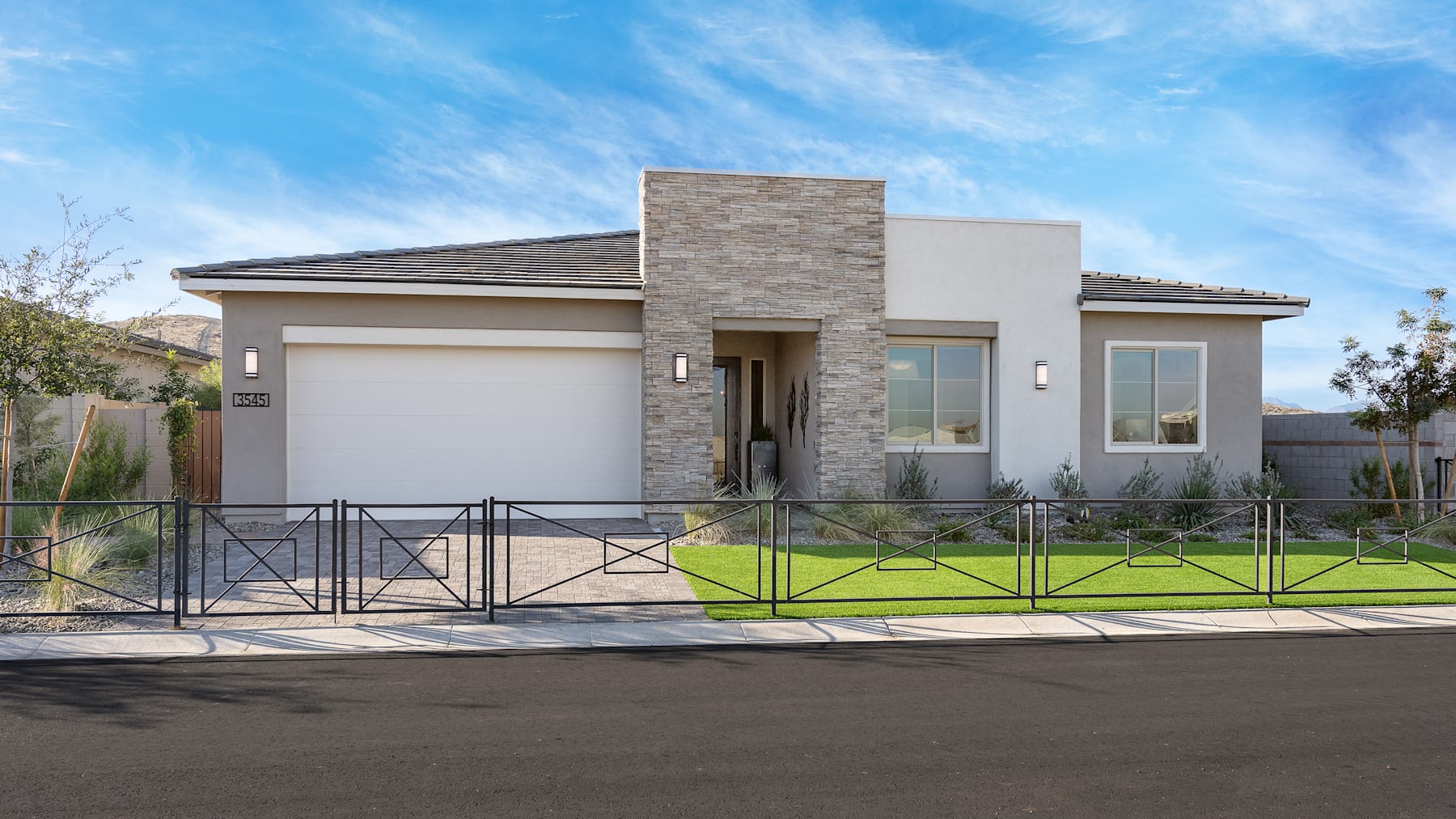 A modern, single-story house with a stone facade, a tiled roof, and a well-manicured lawn in the foreground, set against a clear blue sky with wispy clouds.