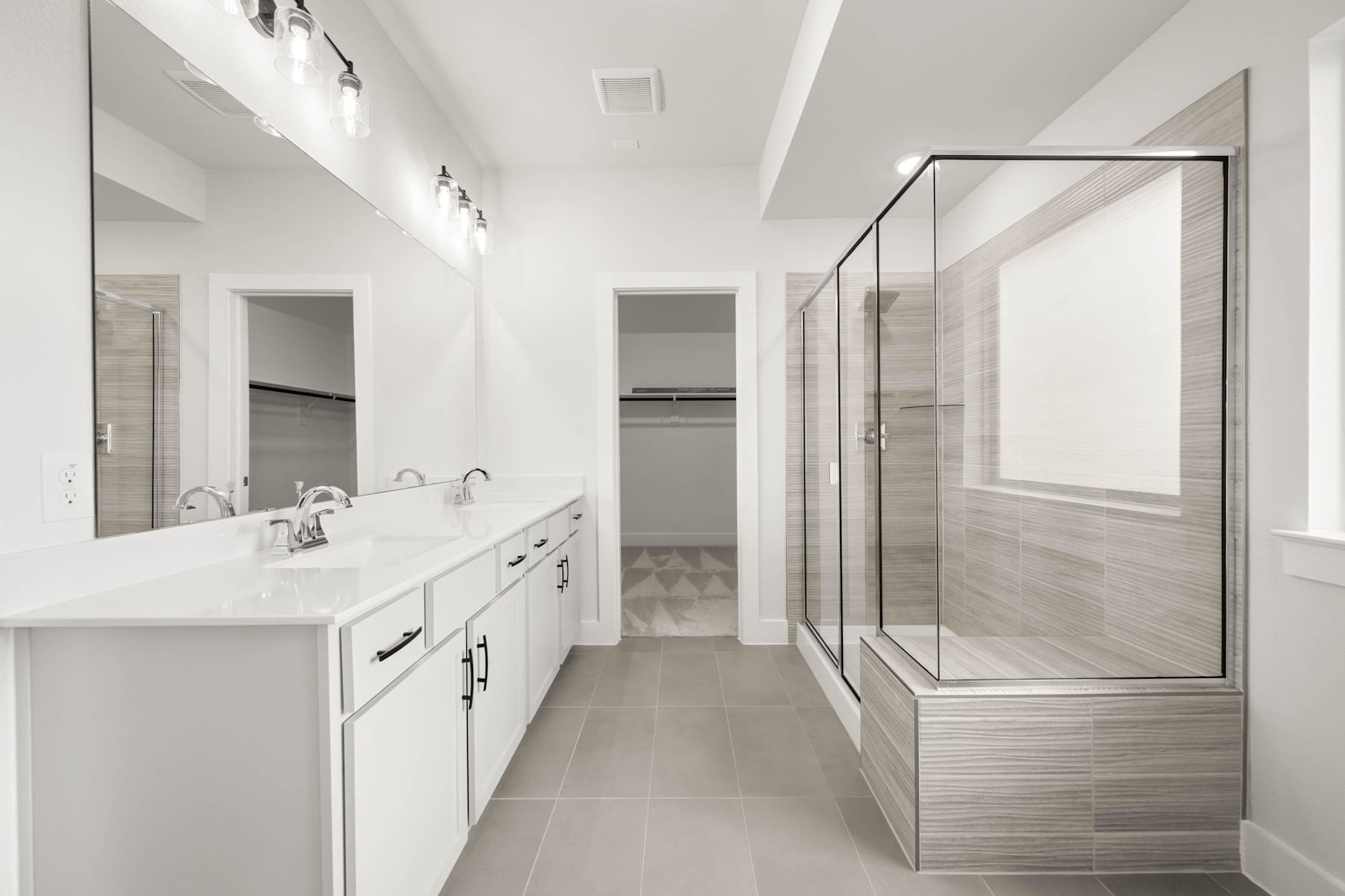 A modern, minimalist bathroom with a white vanity, large mirror, and glass shower enclosure, set against a neutral color palette.