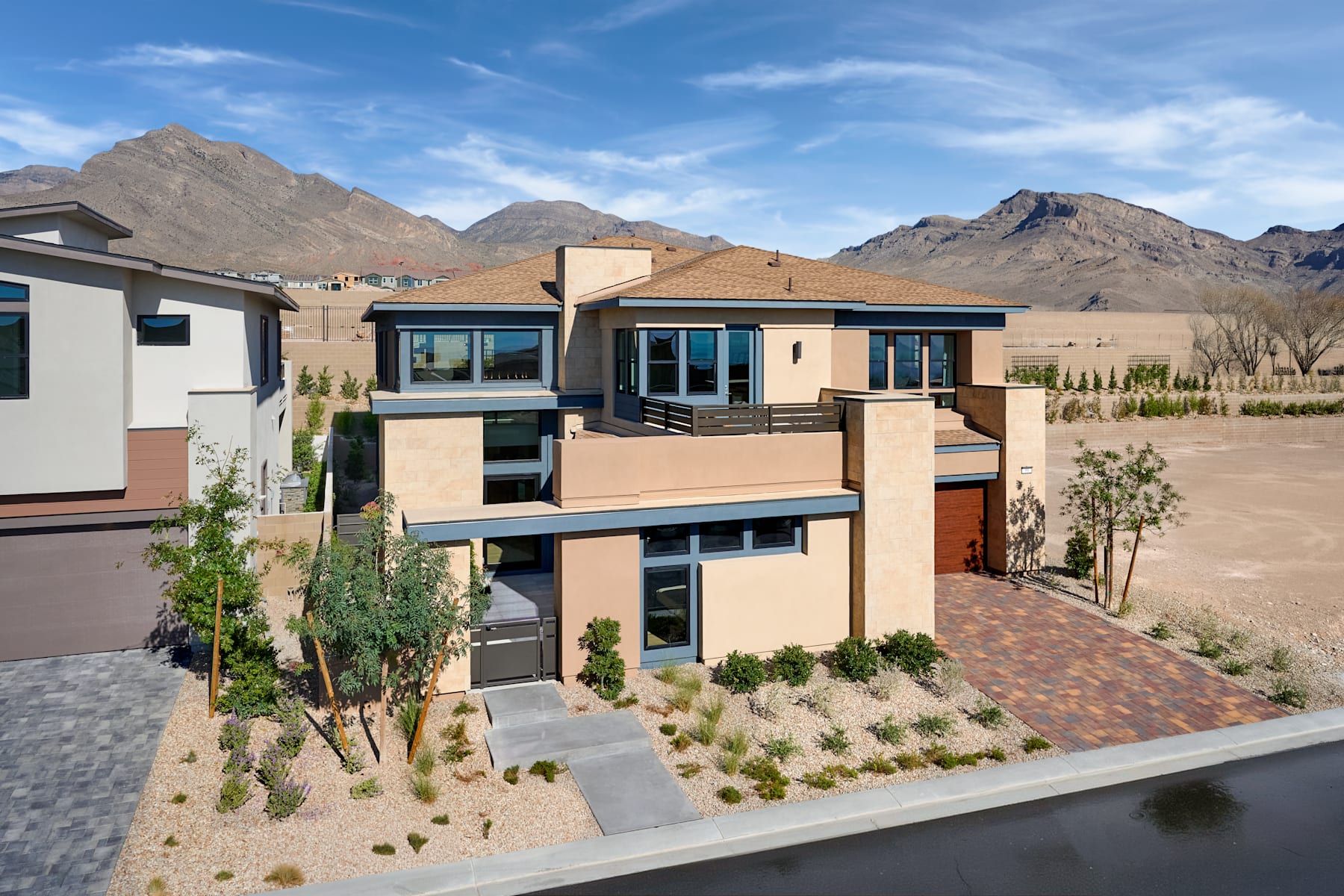 A modern, multi-story residential building nestled among desert landscaping, with mountains visible in the background under a clear blue sky.