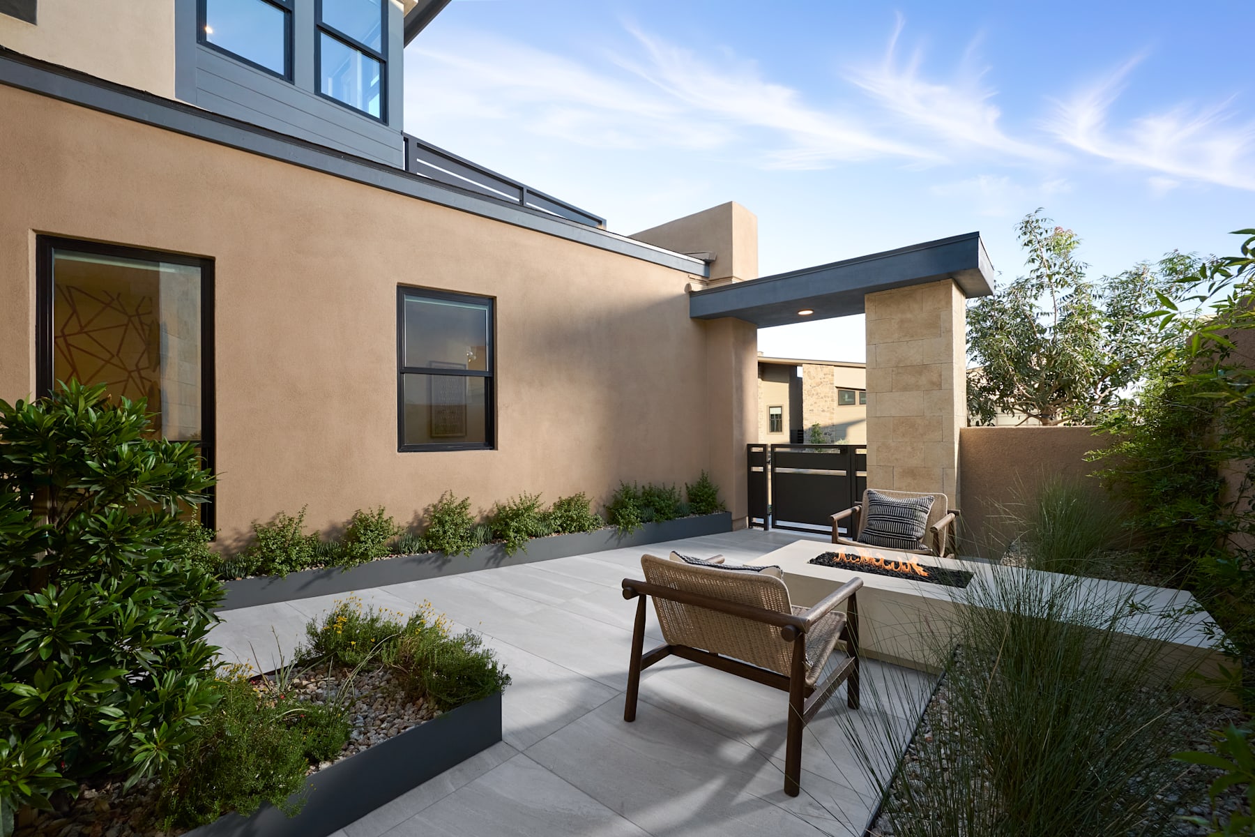 A modern, well-designed outdoor patio area with a wooden bench, surrounded by lush greenery and a clear sky in the background.