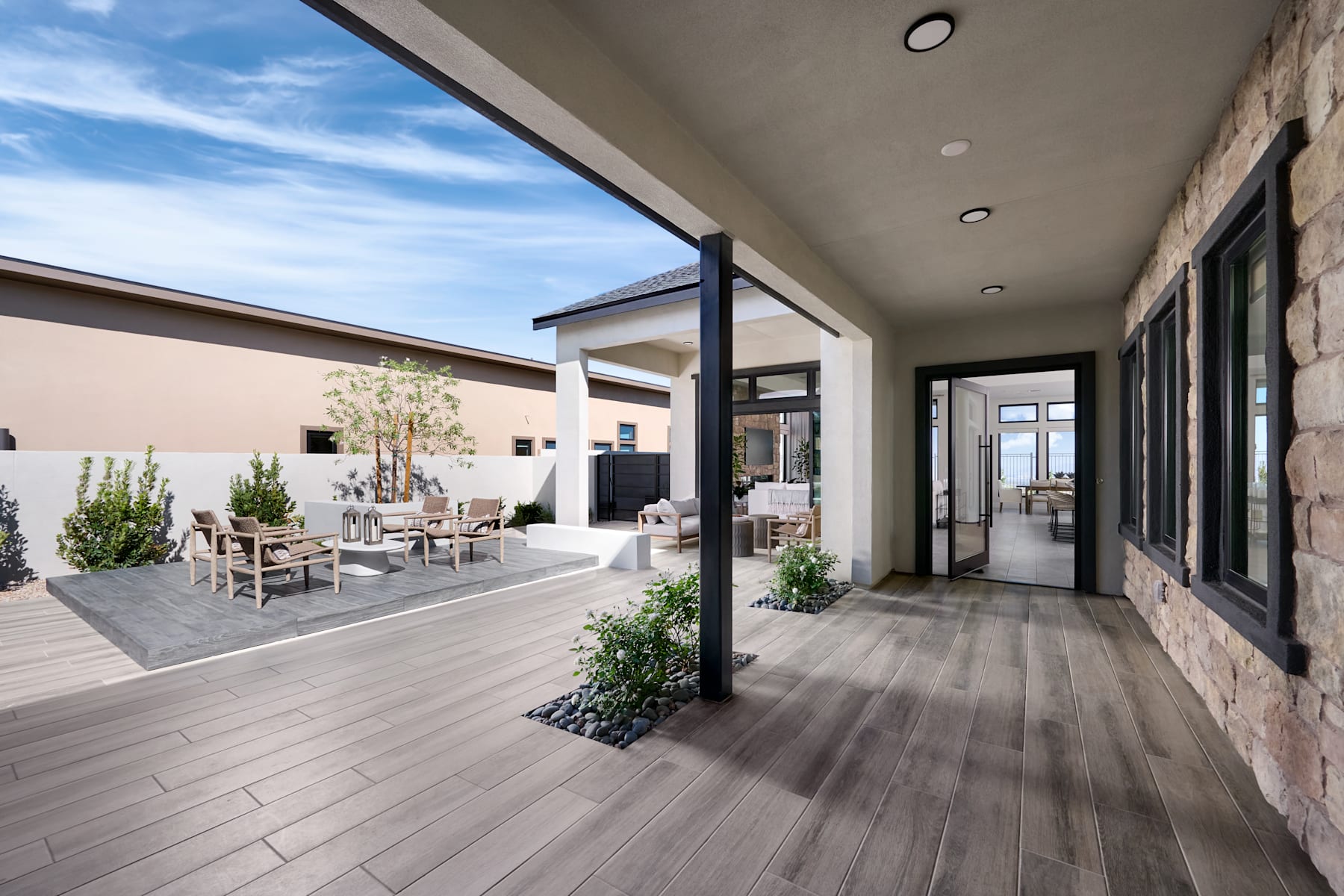 A modern and spacious indoor-outdoor living space with a wooden deck, potted plants, and a view of the sky through large windows.
