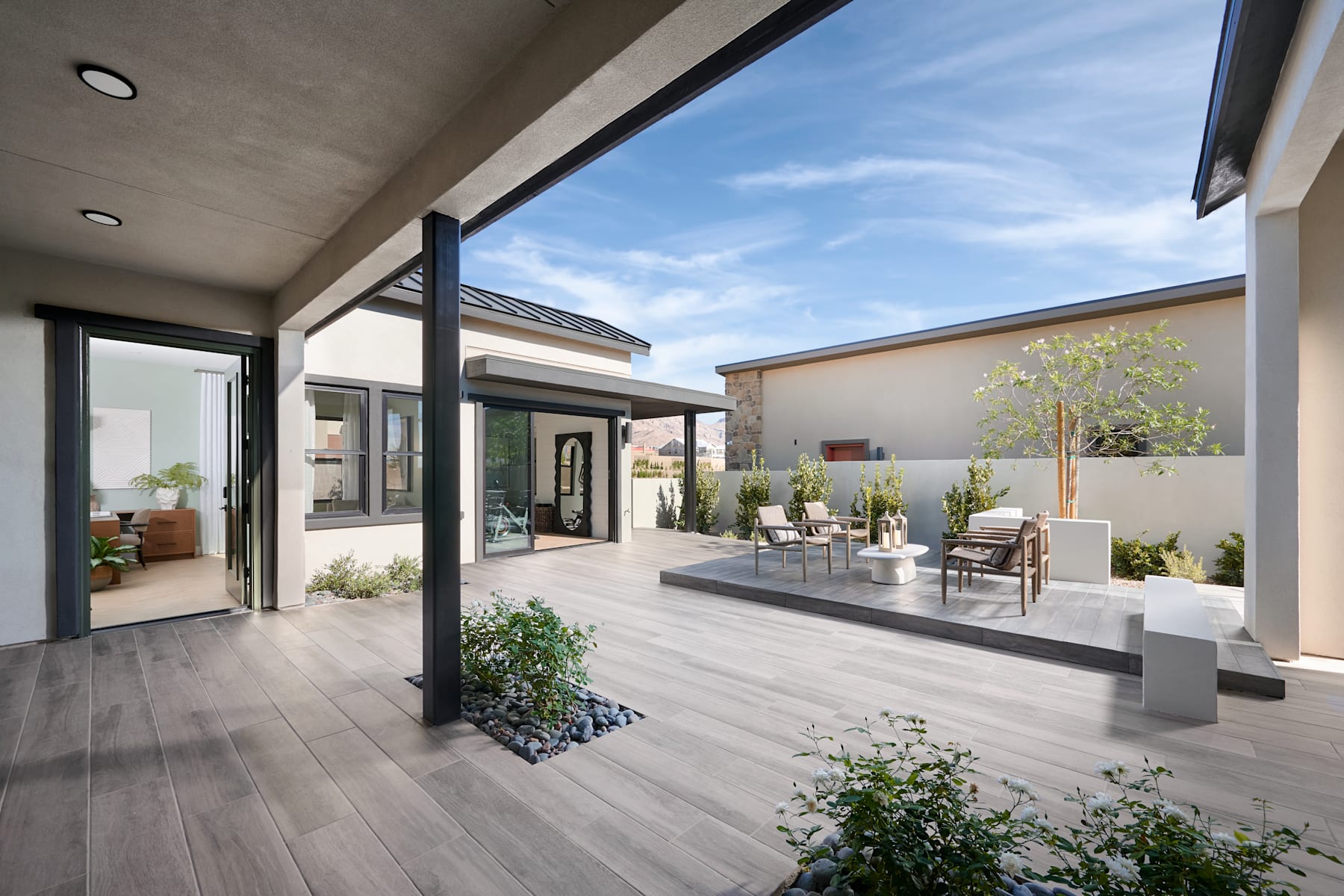 A modern and spacious outdoor living area with a wooden deck, potted plants, and a clear view of the sky through the large windows.