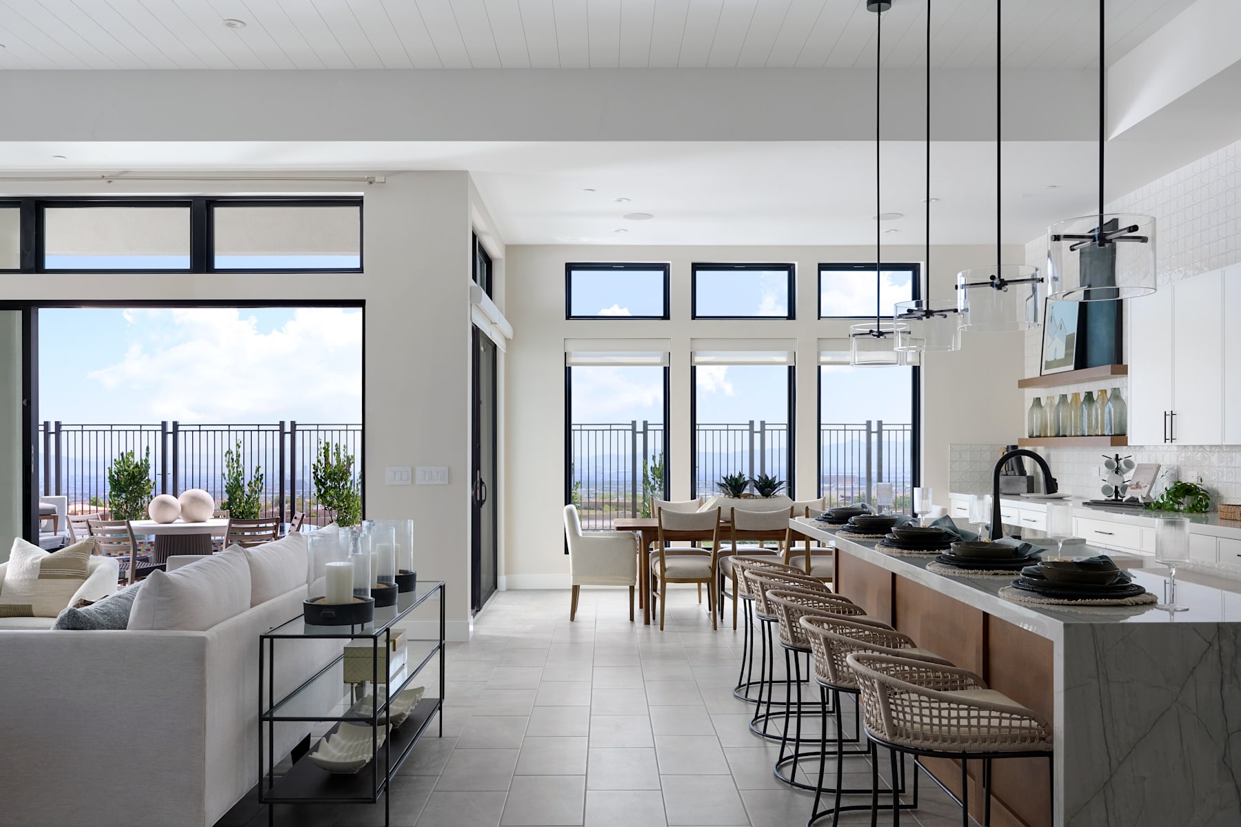 A modern, open-concept kitchen and living room with large windows overlooking a scenic outdoor view, featuring a mix of neutral tones, sleek furniture, and decorative accents.