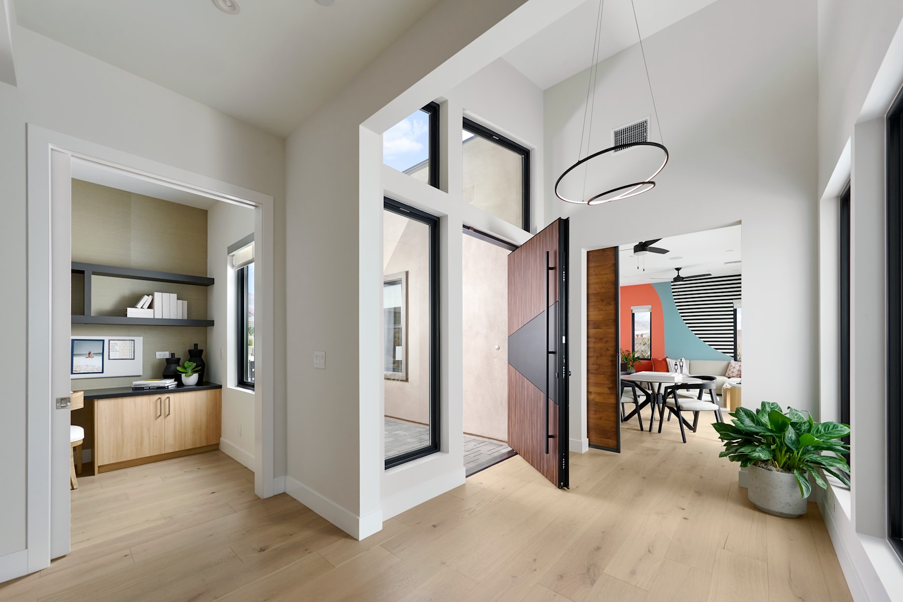 A modern and minimalist hallway with white walls, wooden floors, and various decorative elements such as framed artwork, a potted plant, and a circular light fixture.