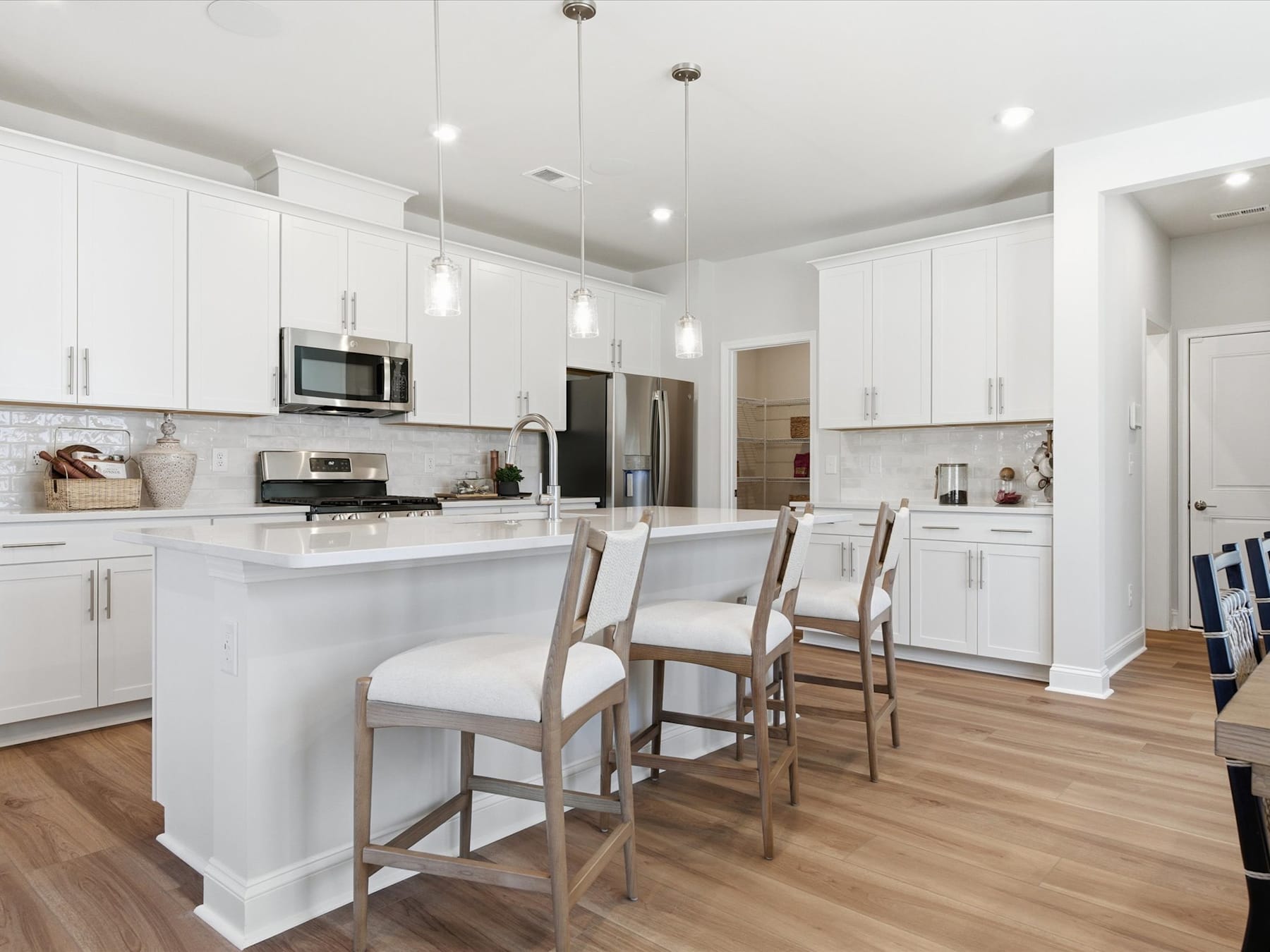 A modern, bright, and spacious kitchen with white cabinets, stainless steel appliances, and wooden bar stools in the foreground.