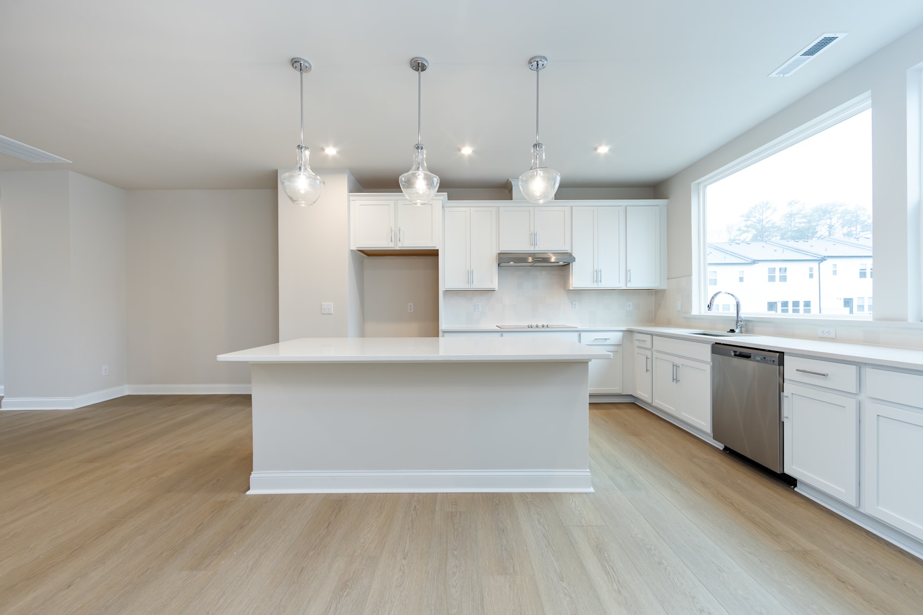 A modern, bright kitchen with white cabinets, a central island, and hardwood floors, illuminated by pendant lights.