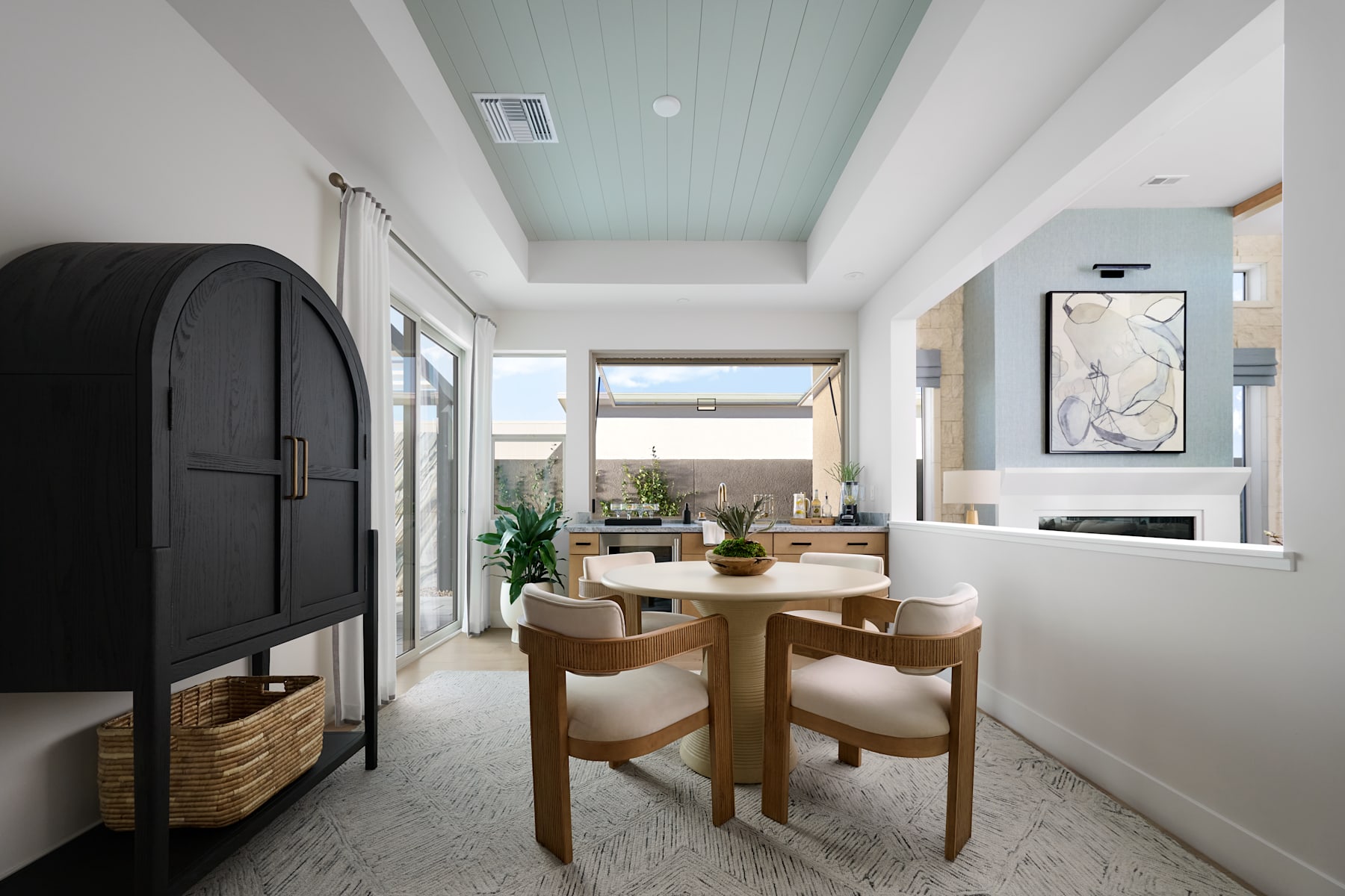 A modern and minimalist dining area with a wooden table and chairs, a fireplace, and a large window overlooking a scenic outdoor view.