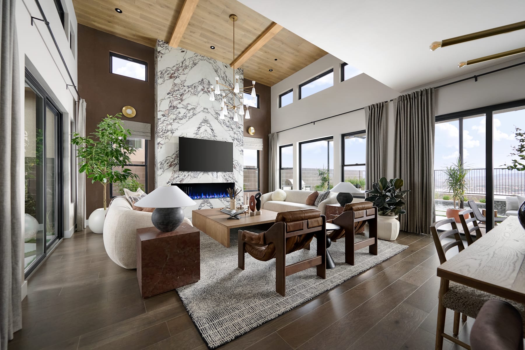 A modern and spacious living room with a fireplace, large windows, and a mix of contemporary and rustic furniture, including a couch, chairs, and a wooden table.