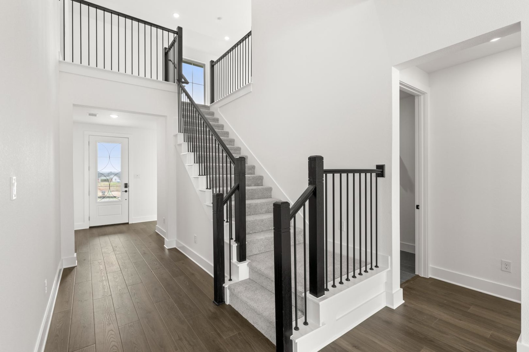 A bright and spacious interior with a wooden staircase, black metal railings, and a view of the outdoors through a doorway.