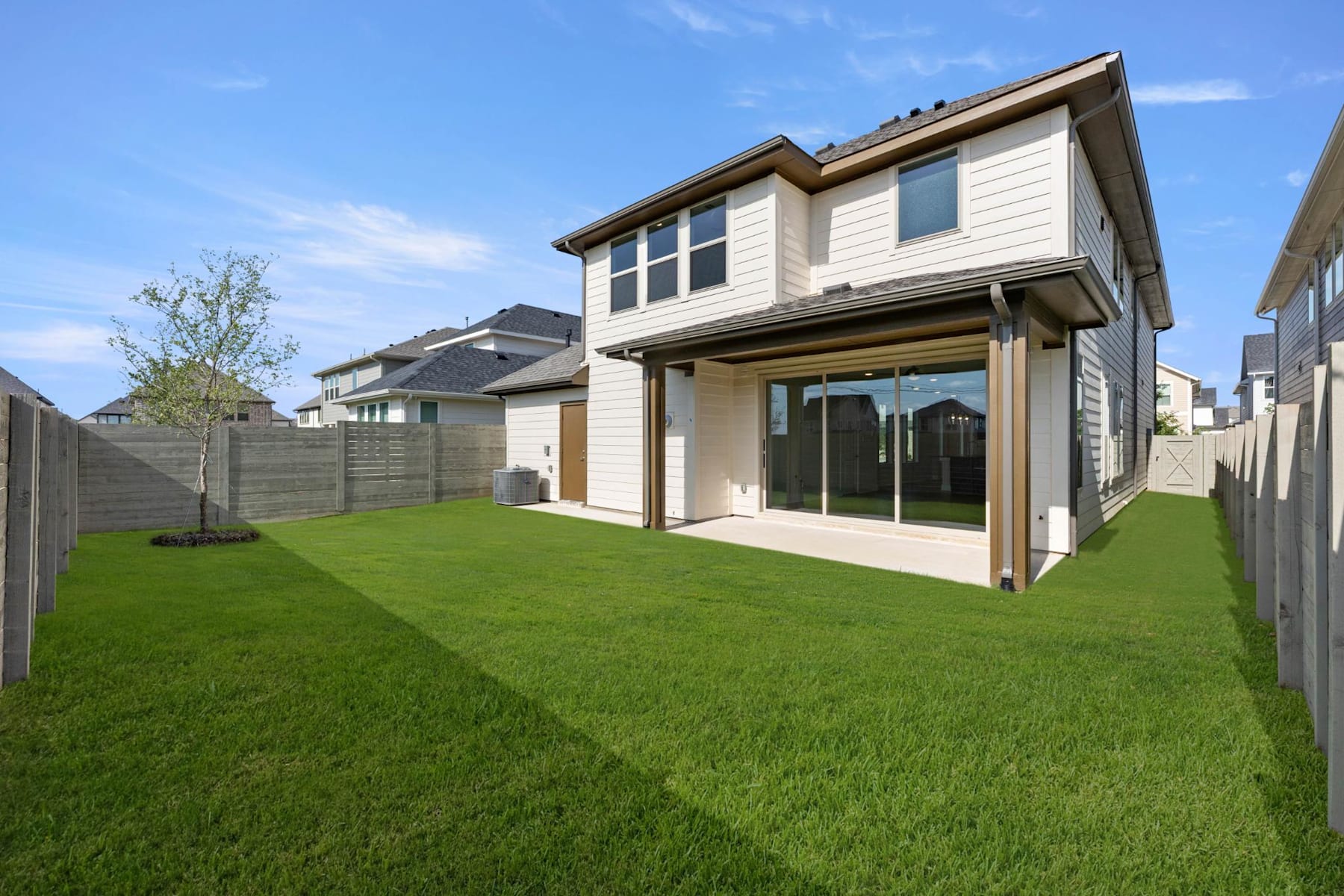 A well-manicured lawn stretches out in the foreground, leading to a modern two-story house with a porch and large windows in the background.