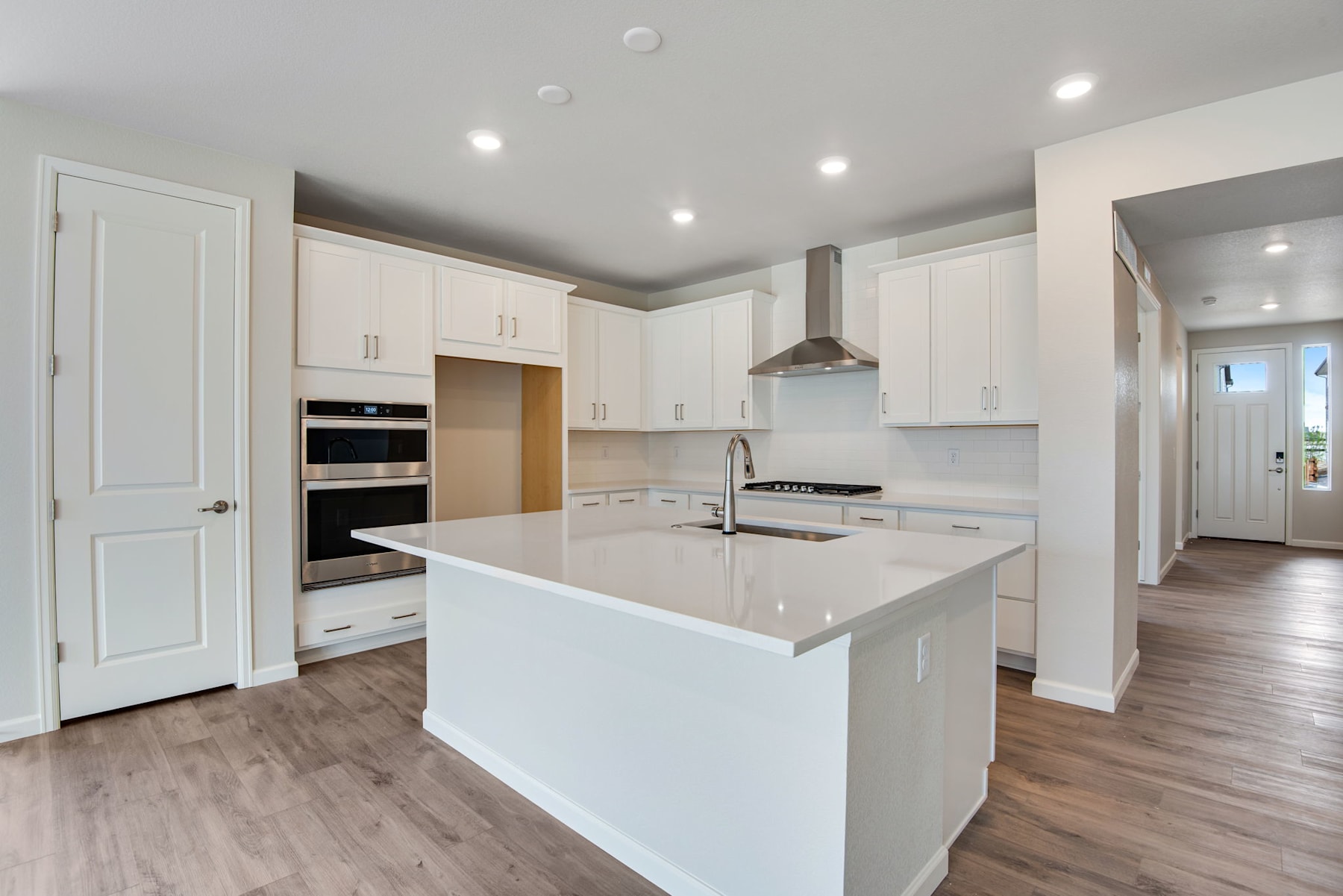 A modern, open-concept kitchen with white cabinets, a large island, and hardwood flooring, creating a bright and spacious atmosphere.