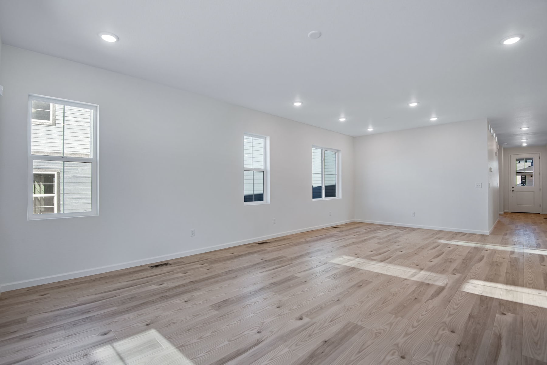 A spacious, well-lit room with hardwood floors, white walls, and recessed lighting fixtures.