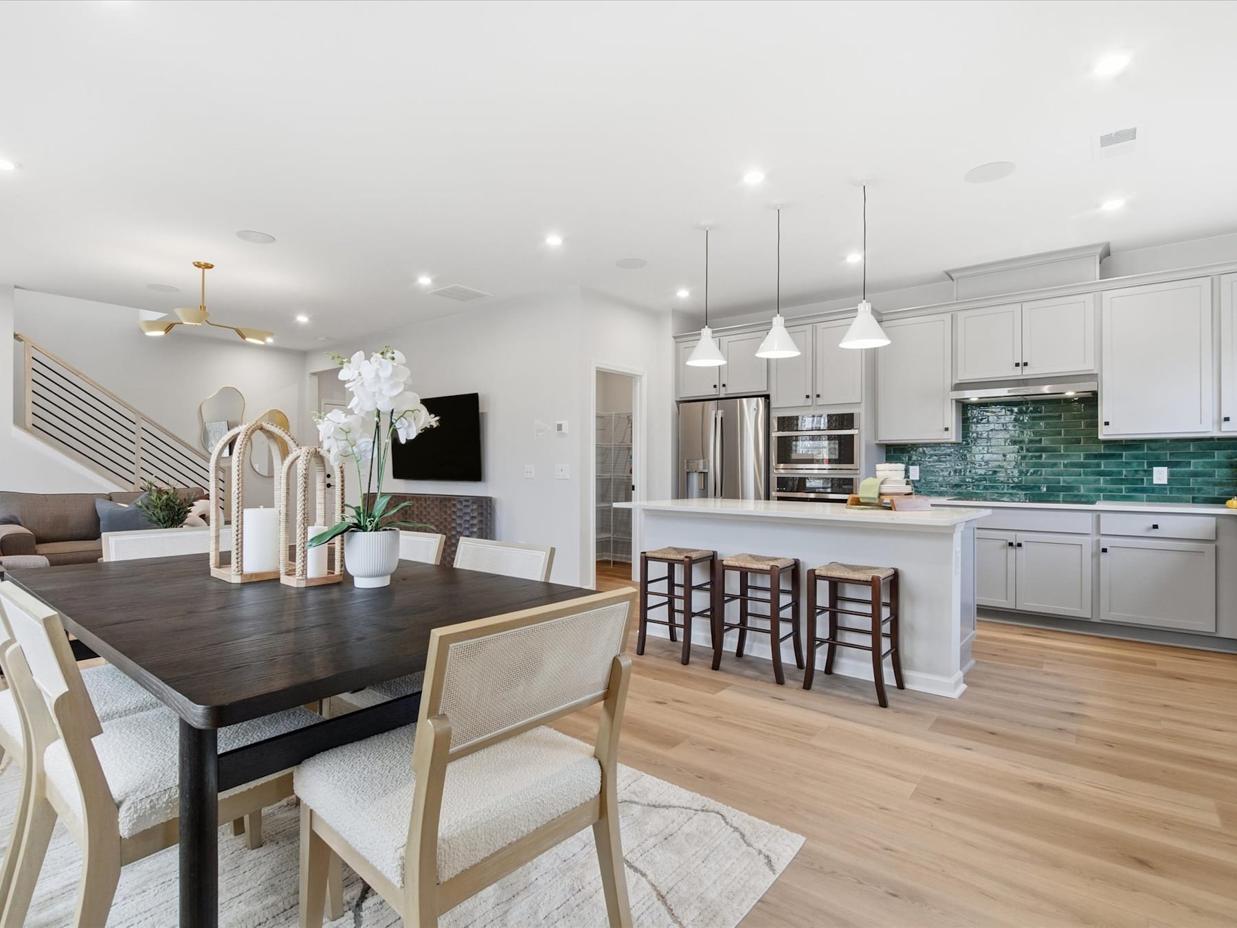 A modern and spacious kitchen and dining area with white cabinets, a dark wooden dining table, and hardwood floors.