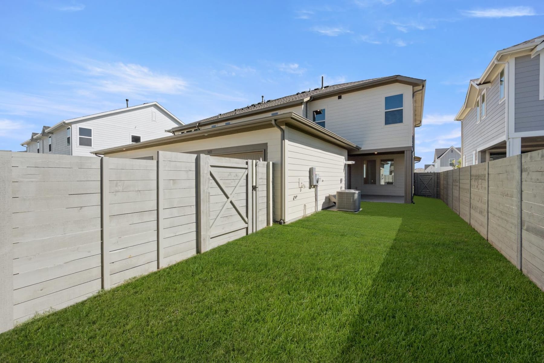 A well-maintained backyard with a lush green lawn, surrounded by a white fence and neighboring houses in the background.