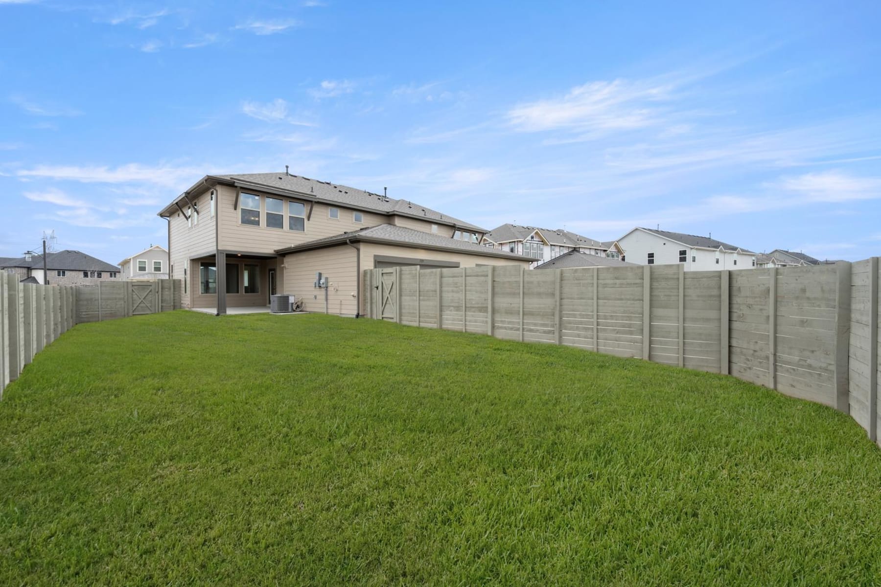 A well-manicured lawn stretches out in the foreground, leading to a row of houses with wooden fences in the background under a clear blue sky.