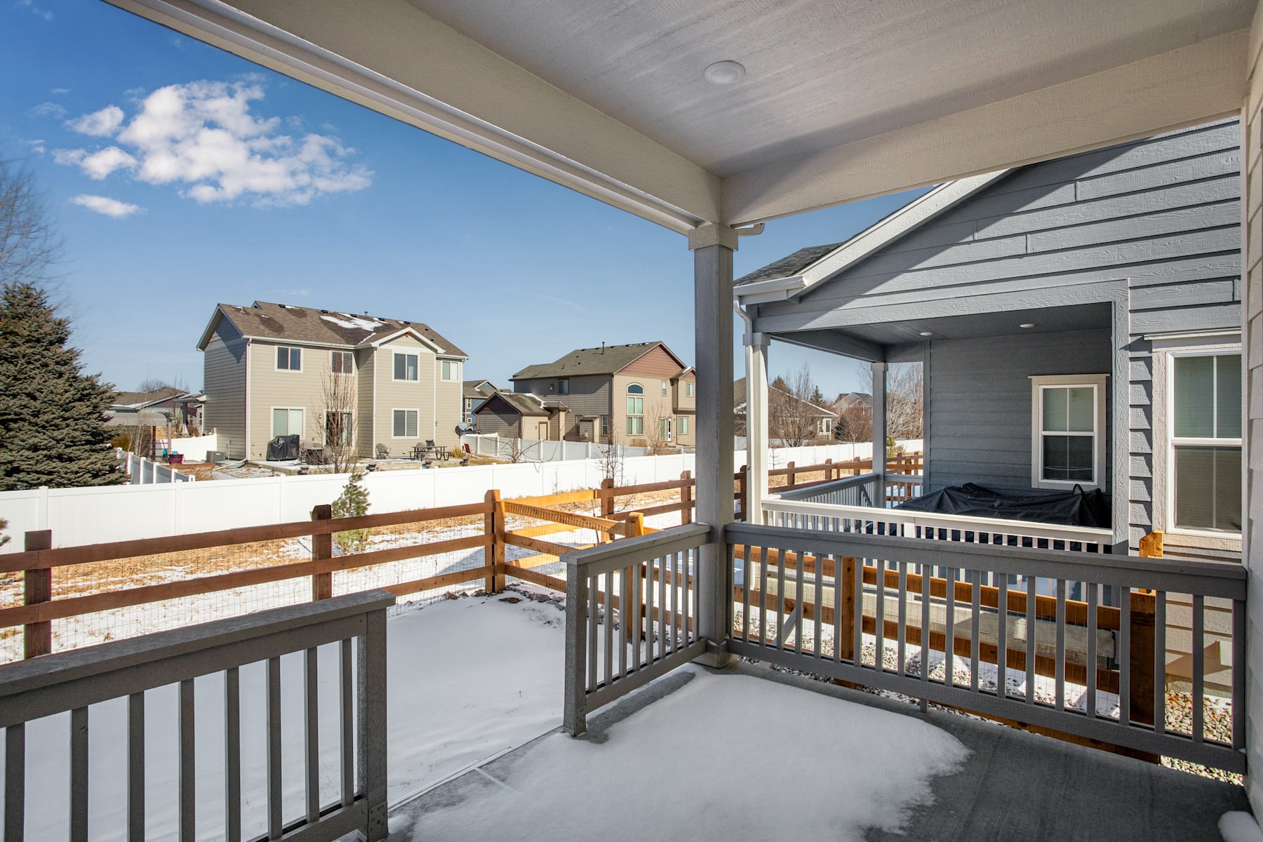A snow-covered residential neighborhood with a wooden deck and railing in the foreground, overlooking a scenic winter landscape in the background.