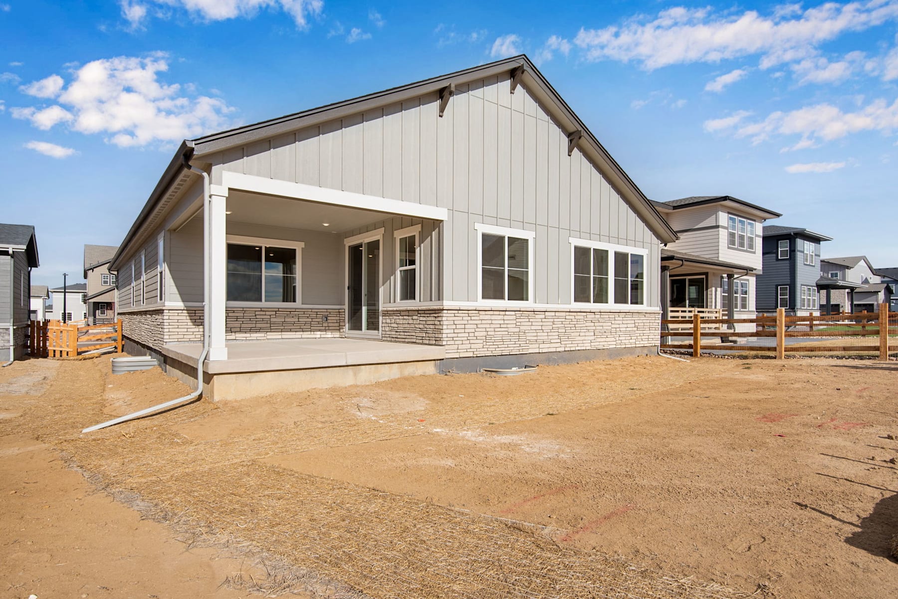A newly constructed single-story residential building with a porch and a gravel-covered yard in the foreground, set against a blue sky with scattered clouds.