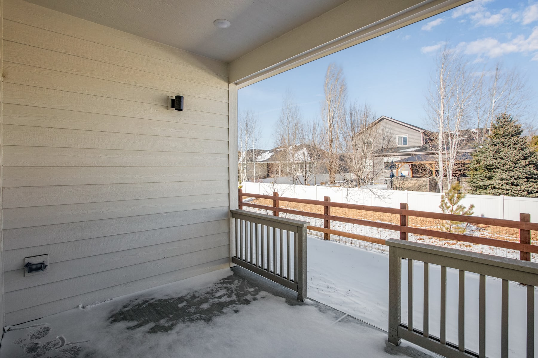 A snow-covered porch with a wooden railing overlooks a residential neighborhood in the background, with bare trees and houses visible through the window.
