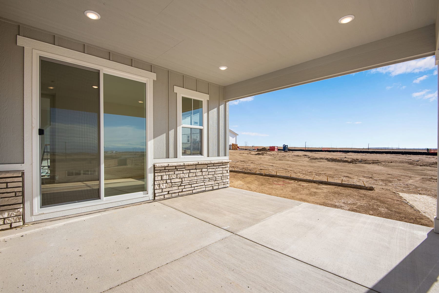 A spacious patio with large windows overlooking an open, rural landscape with a clear blue sky in the background.