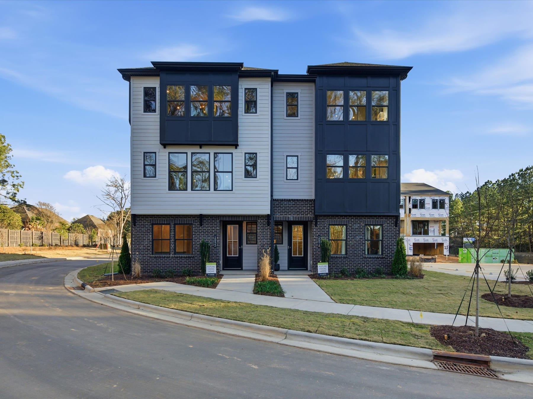 A modern, multi-story townhouse complex with a gray exterior, surrounded by a grassy lawn and trees in the background.