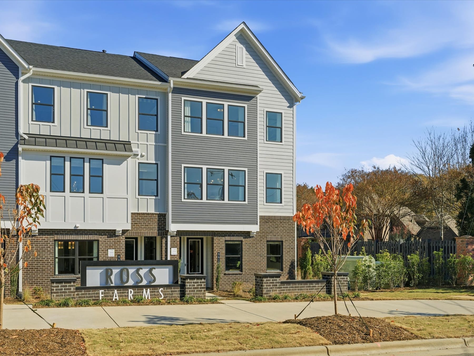 A multi-story residential building with a brick and siding exterior, surrounded by trees and landscaping, with a sign for "Ross Farms" in the foreground.