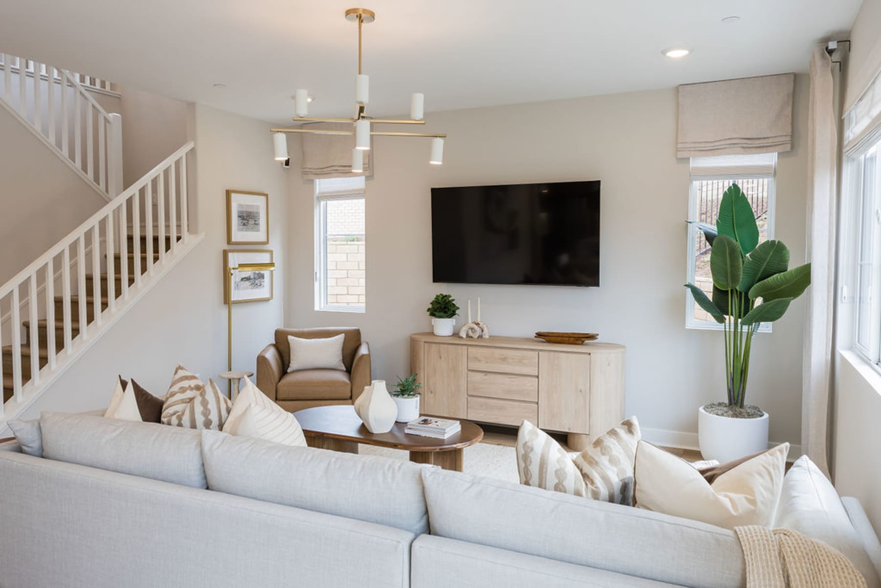 A cozy and inviting living room with a large white sofa, a wooden cabinet, and a TV mounted on the wall, complemented by decorative elements such as plants and artwork.