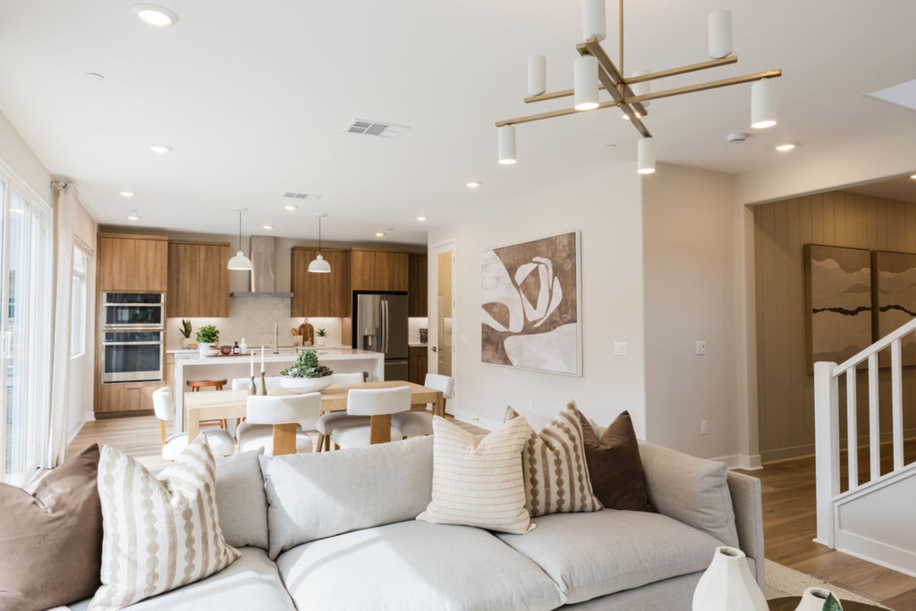 A modern and cozy open-concept living space with a comfortable sofa, a dining area, and a kitchen with wooden cabinetry and a unique light fixture.