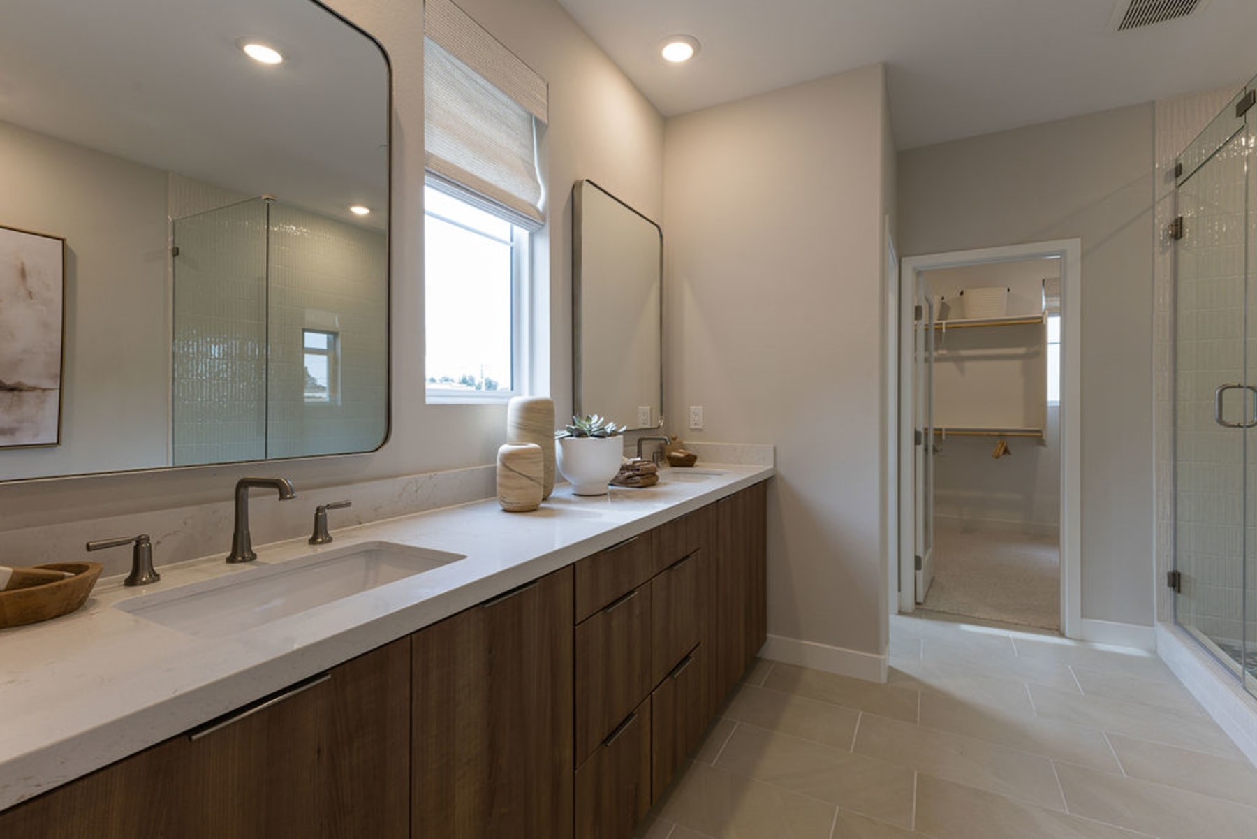 A modern and spacious bathroom with a large vanity, double sinks, and a glass-enclosed shower area, all bathed in natural light from the window.