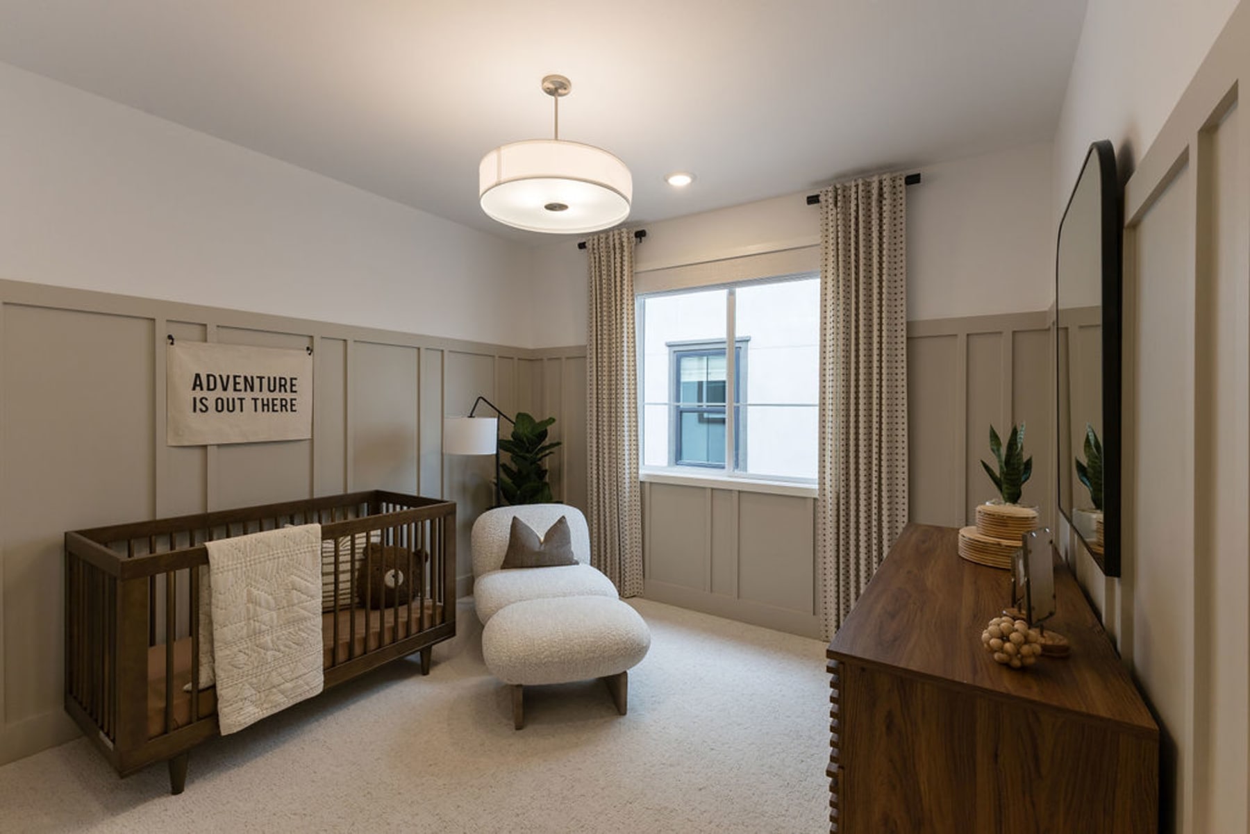 A cozy and modern nursery room with a wooden crib, a plush chair, and various decorative elements such as plants and a wall sign.