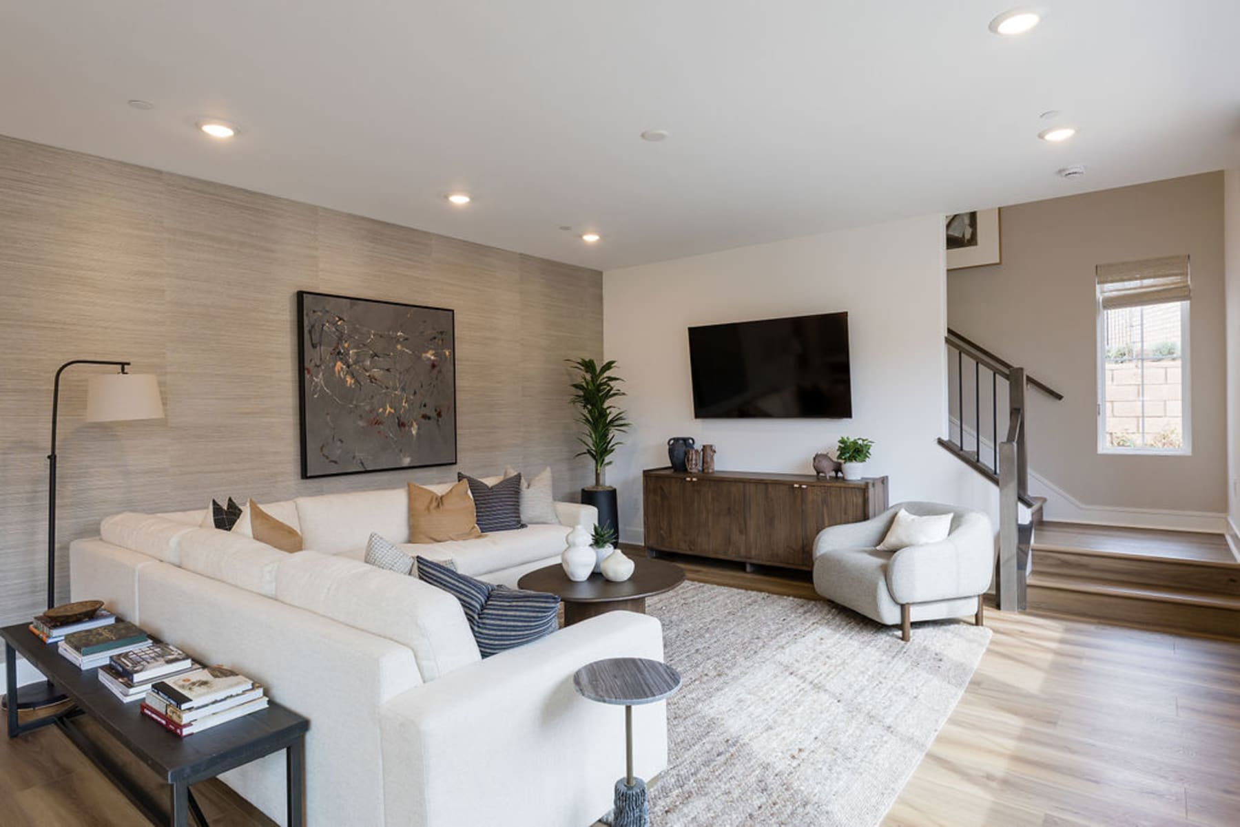 A cozy and modern living room with a white sofa, a wooden cabinet, and a large abstract artwork on the wall, set against a neutral color scheme and hardwood floors.