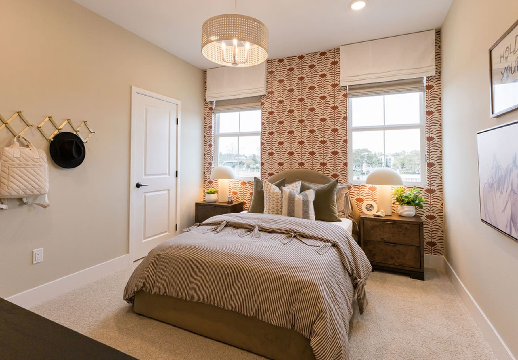 A cozy and well-decorated bedroom with a patterned accent wall, a wooden dresser, and a comfortable-looking bed with neutral bedding.