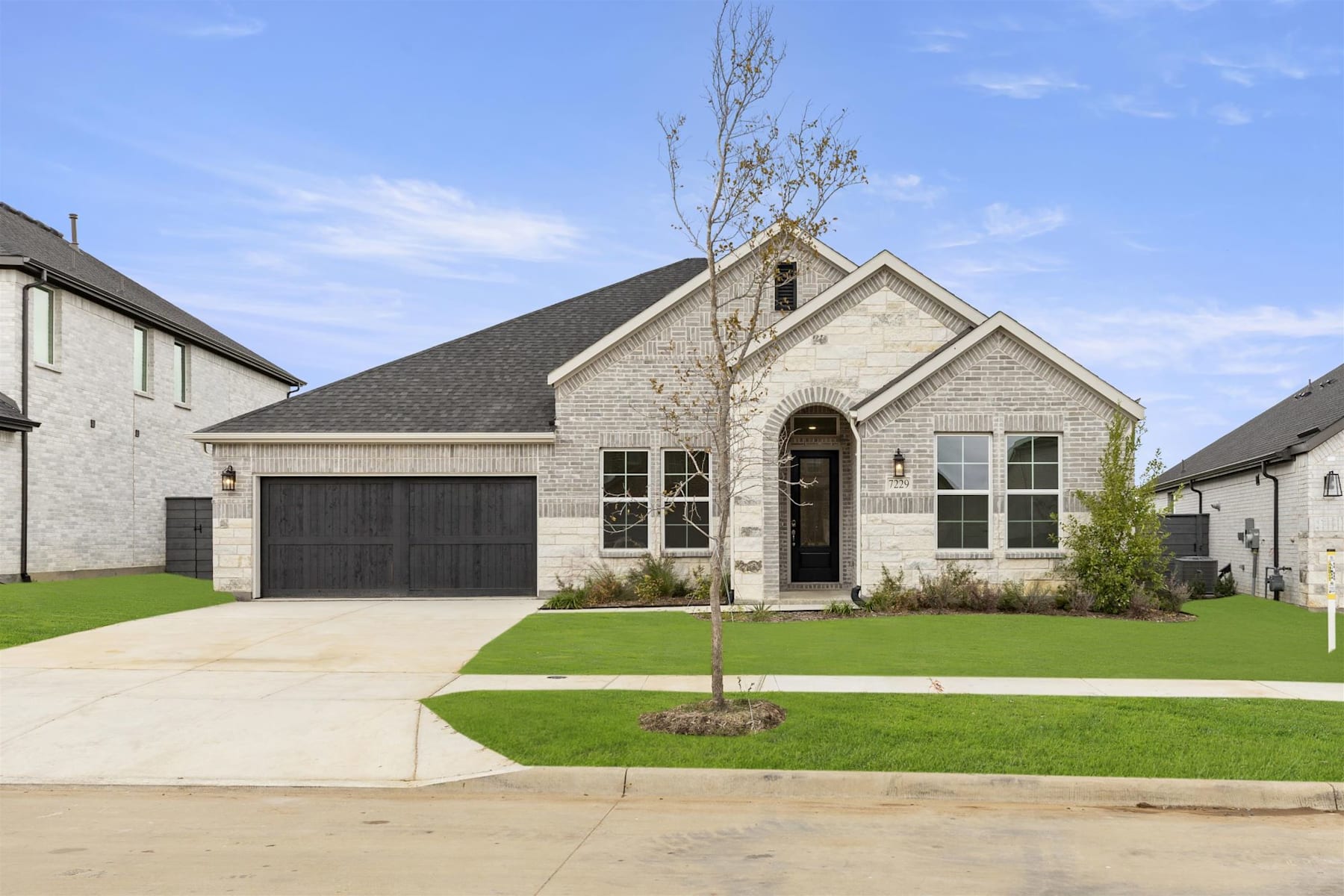 A newly constructed two-story house with a garage, surrounded by a well-manicured lawn and situated in a residential neighborhood.