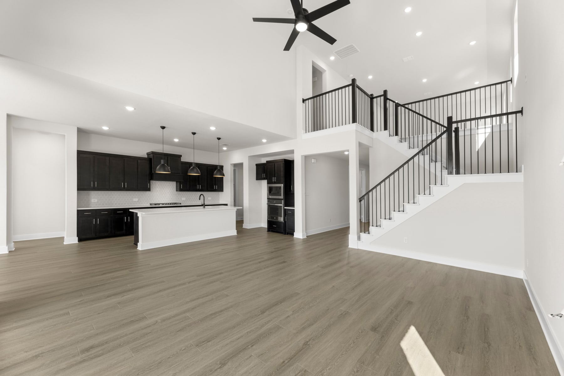 A modern, open-concept living space with a kitchen, staircase, and hardwood flooring, featuring a black and white color scheme and sleek, minimalist design elements.