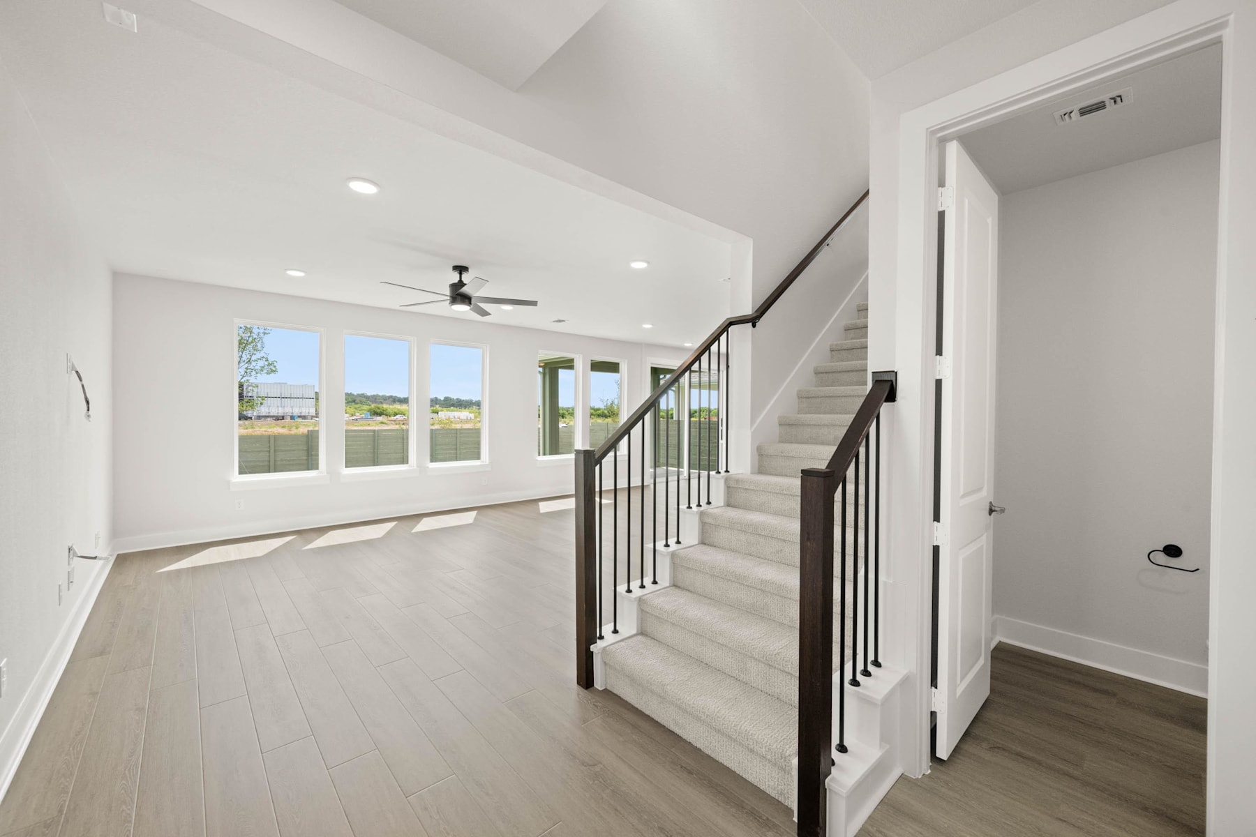 A spacious, bright, and modern interior with a staircase, hardwood floors, and large windows overlooking the outdoor scenery.