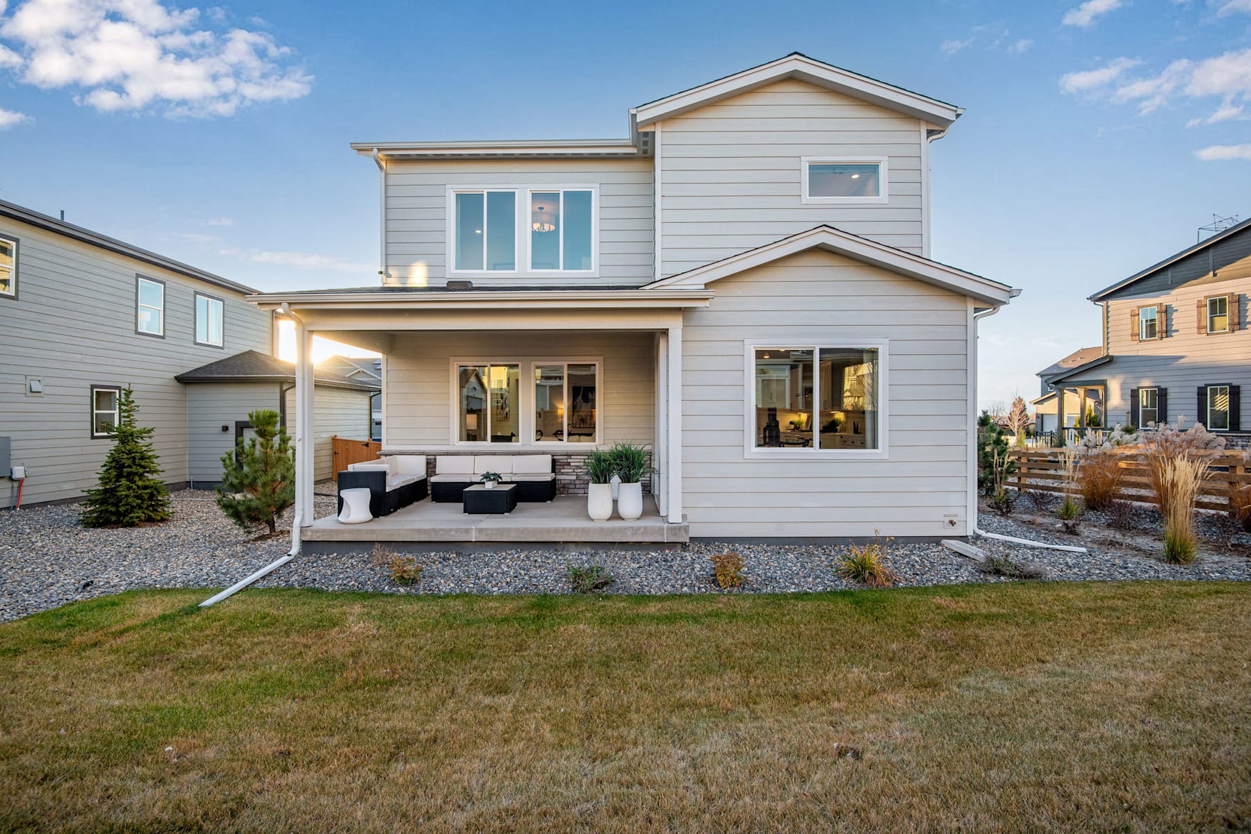 A modern two-story house with a porch and landscaped yard, set against a clear blue sky with scattered clouds.