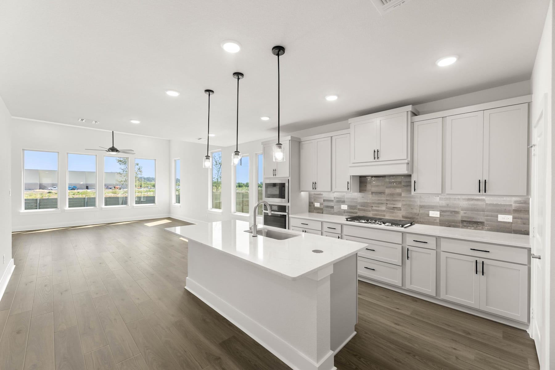 A modern, bright, and spacious kitchen with white cabinets, a kitchen island, and pendant lighting fixtures, overlooking a scenic outdoor view through large windows.