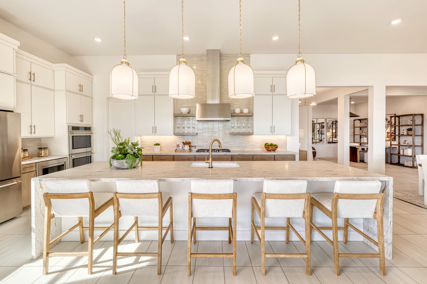 A spacious and modern kitchen with white cabinets, a large island with bar stools, and pendant lighting fixtures hanging from the ceiling.