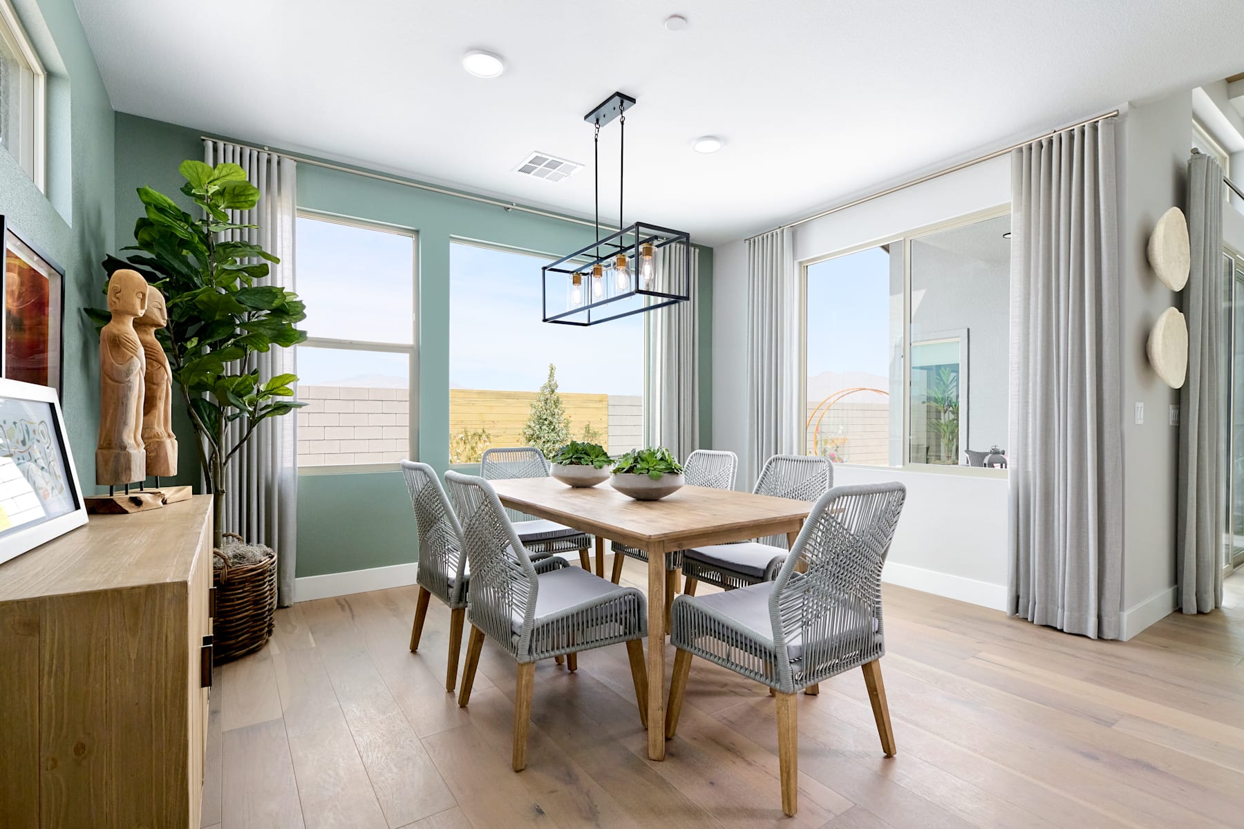 A modern and bright dining room with a wooden table, gray upholstered chairs, and a large window overlooking a scenic outdoor landscape.
