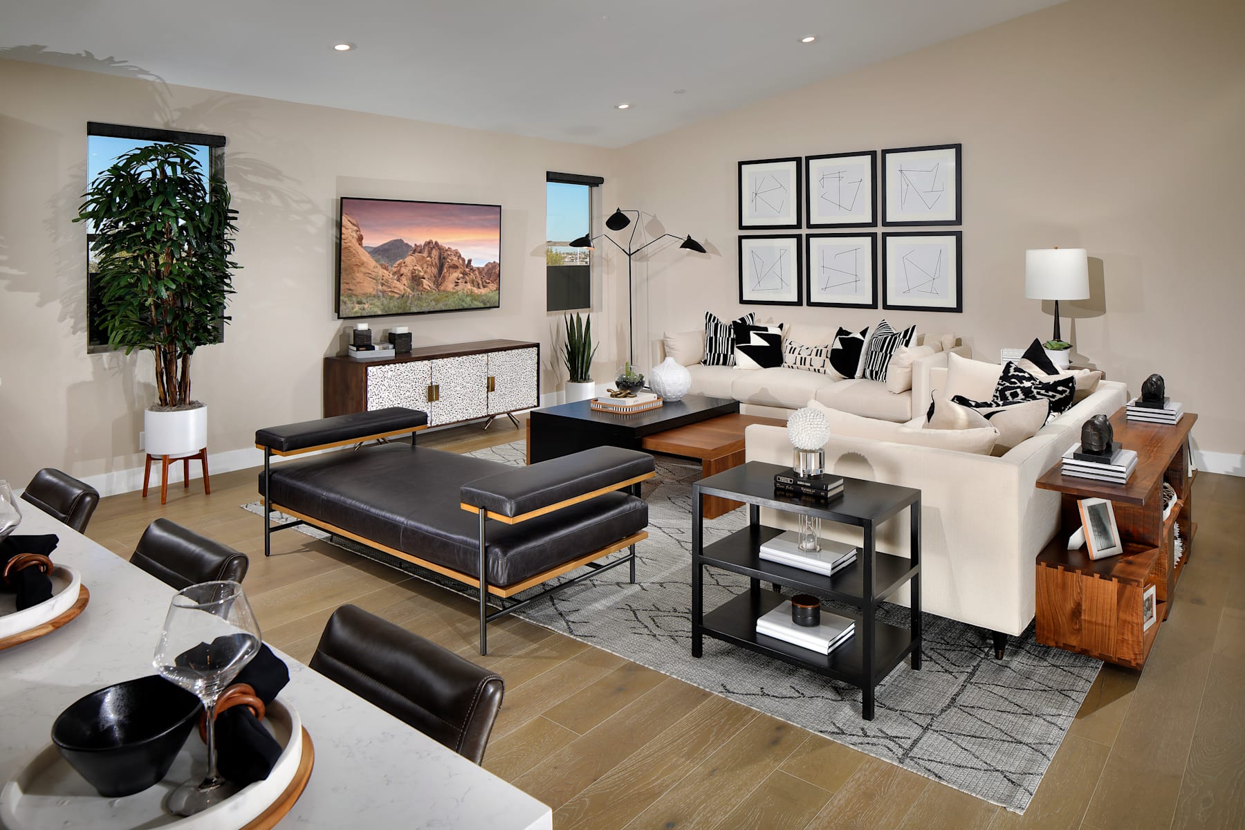 A modern and stylish living room with a large white sofa, black accent chairs, and a patterned area rug on a hardwood floor. The room features large windows with a scenic landscape visible in the background.