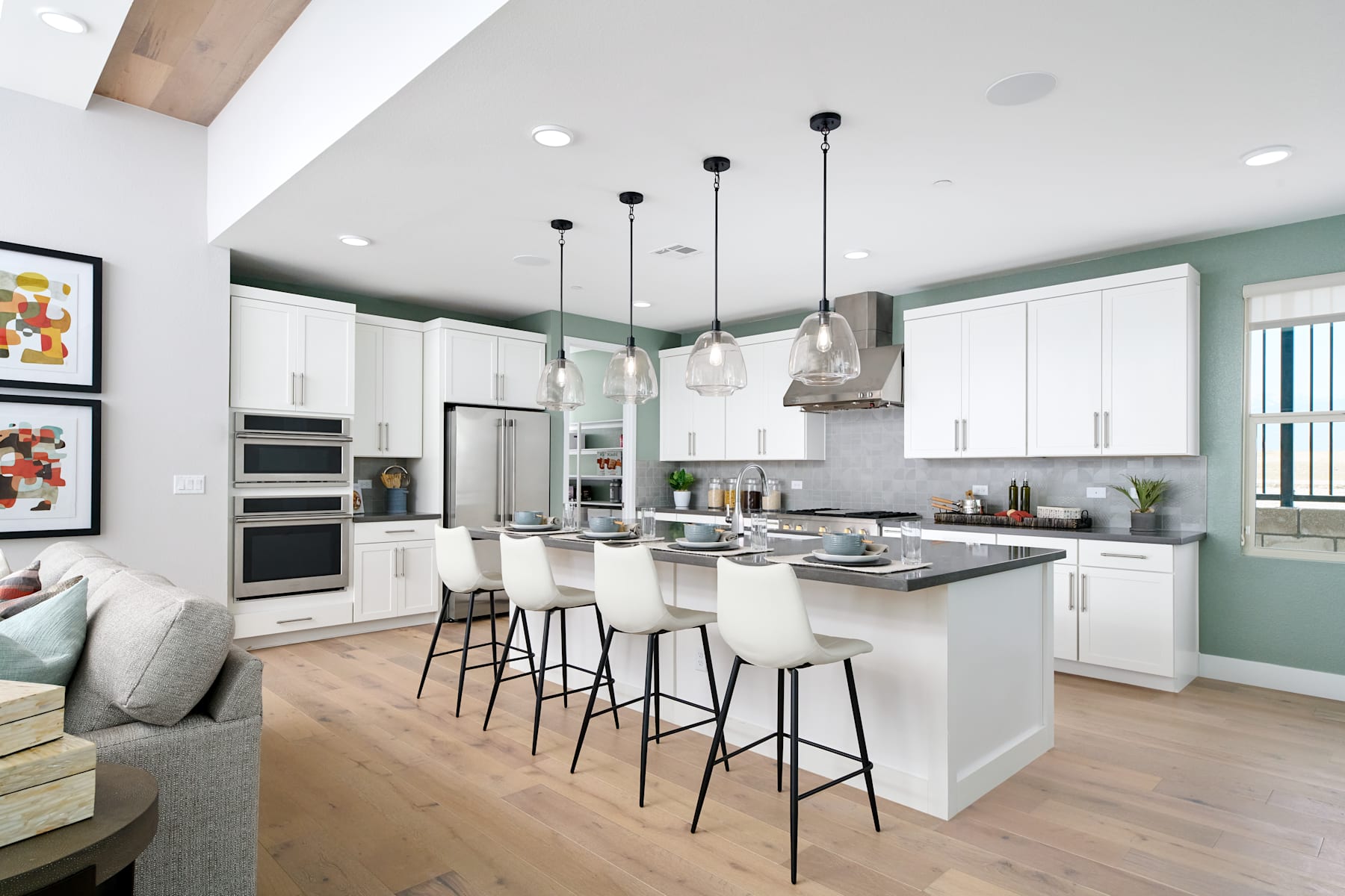 A modern, open-concept kitchen with white cabinets, a large island, and pendant lighting fixtures, set against a neutral color palette and accented with artwork on the walls.