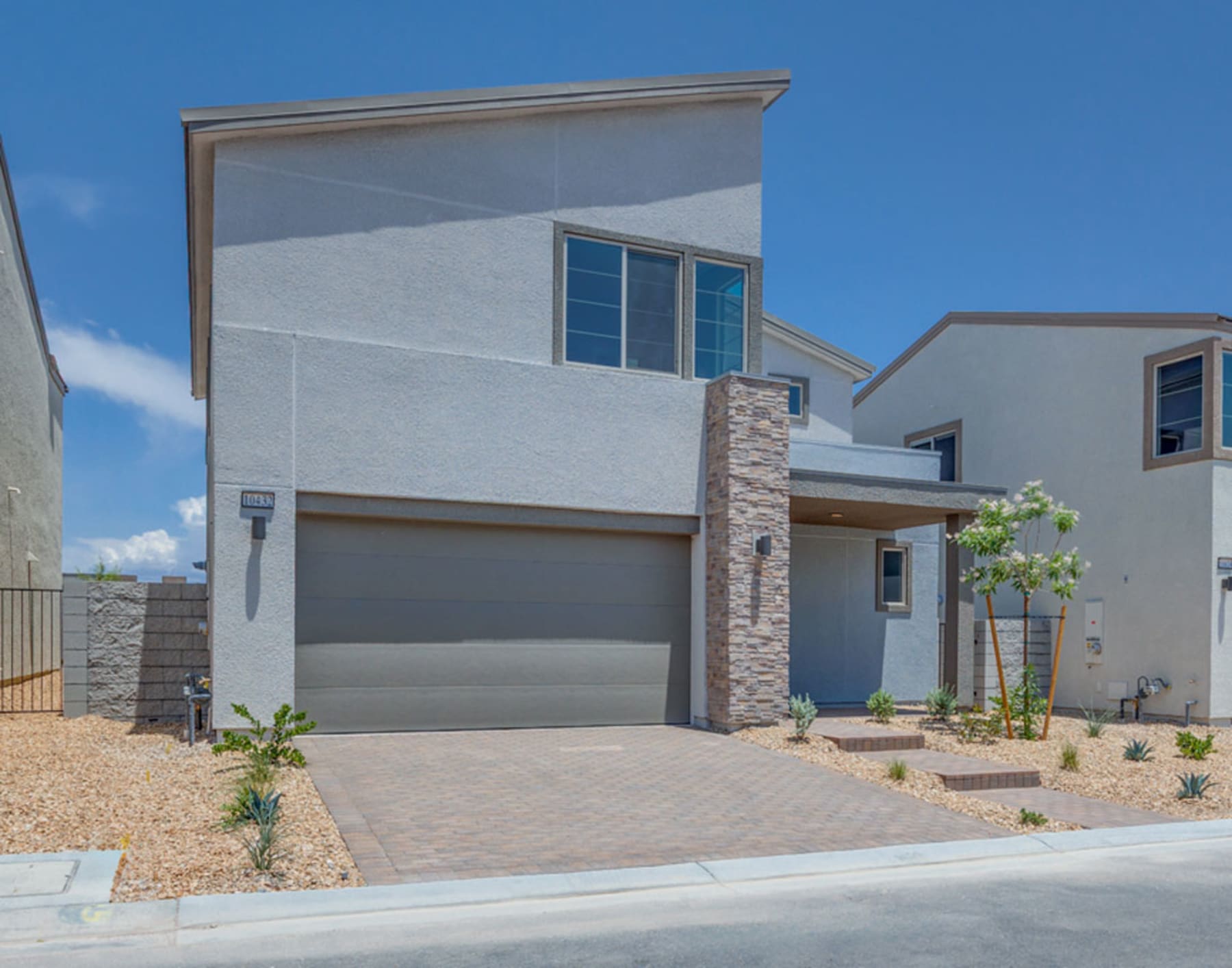 A modern two-story house with a garage, stone accents, and a well-landscaped front yard against a clear blue sky.