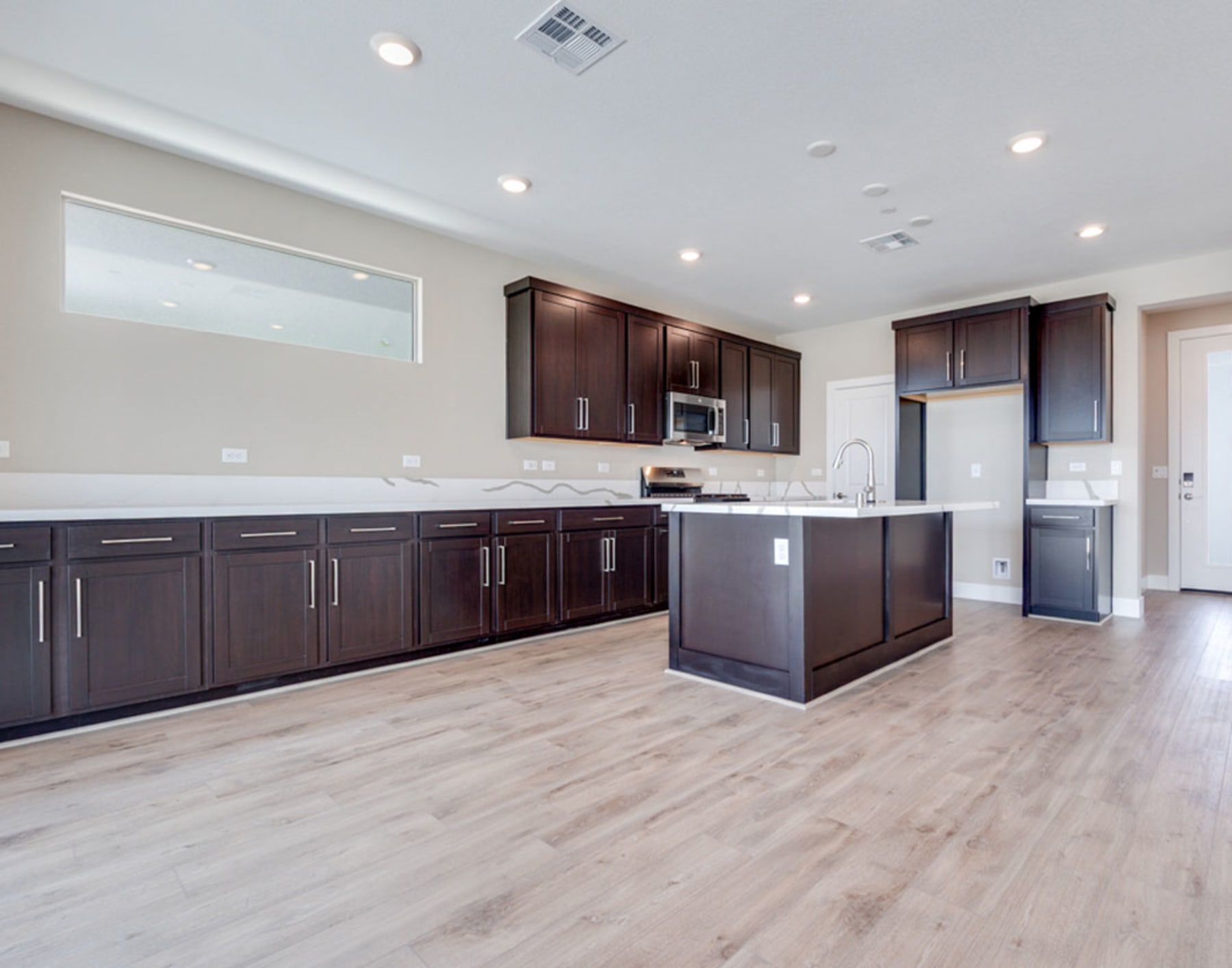 A modern, spacious kitchen with dark wood cabinets, stainless steel appliances, and a light-colored hardwood floor.